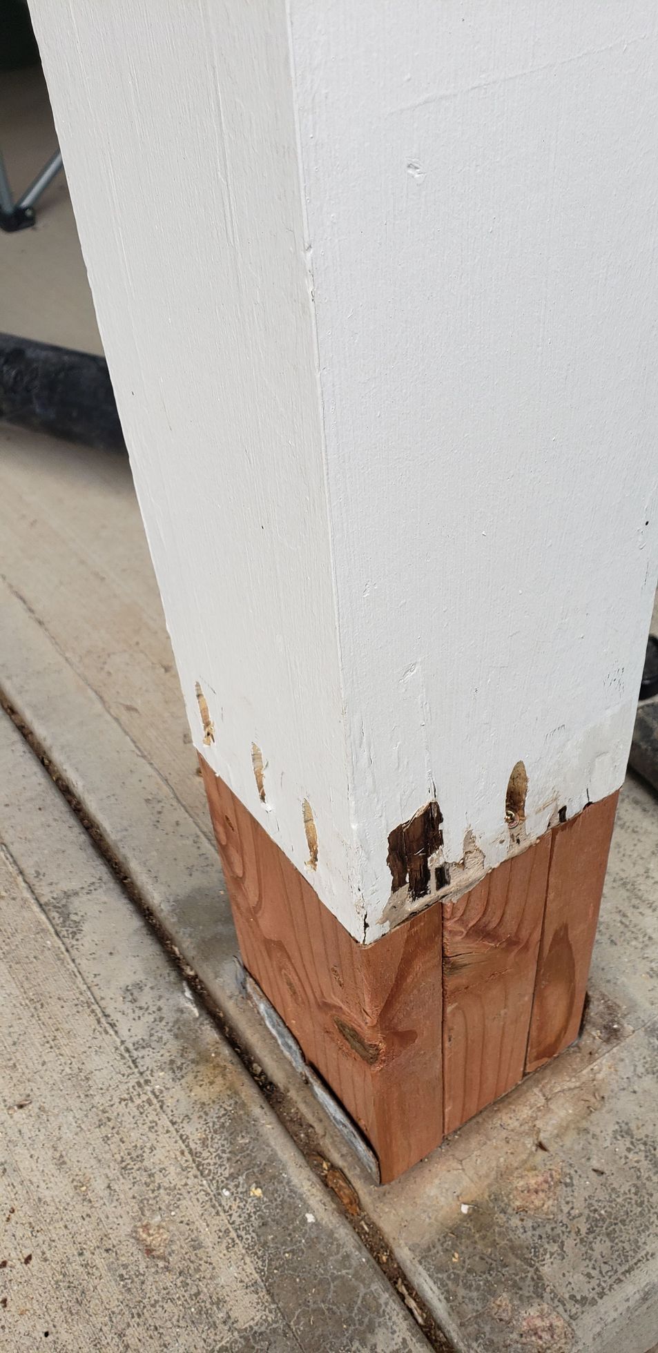 White porch post with peeling paint and exposed wood at the base near a concrete walkway.