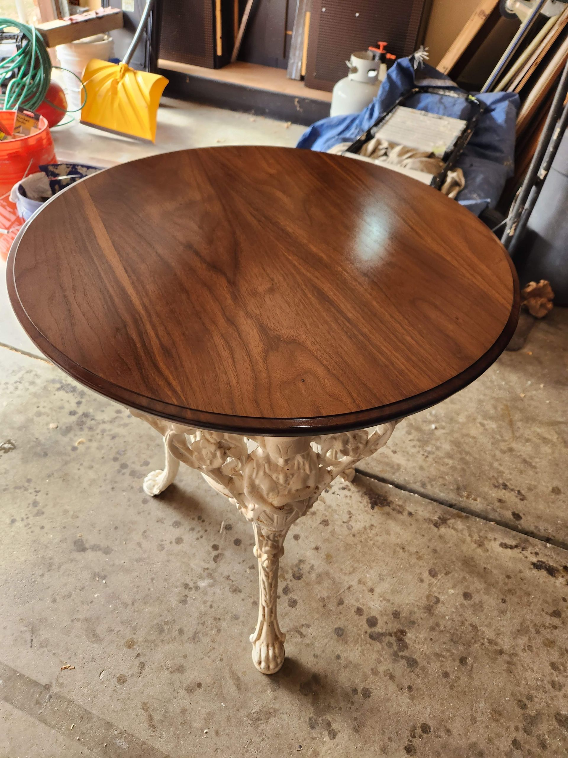 Round wood table with white carved pedestal base on a concrete floor in a cluttered room.