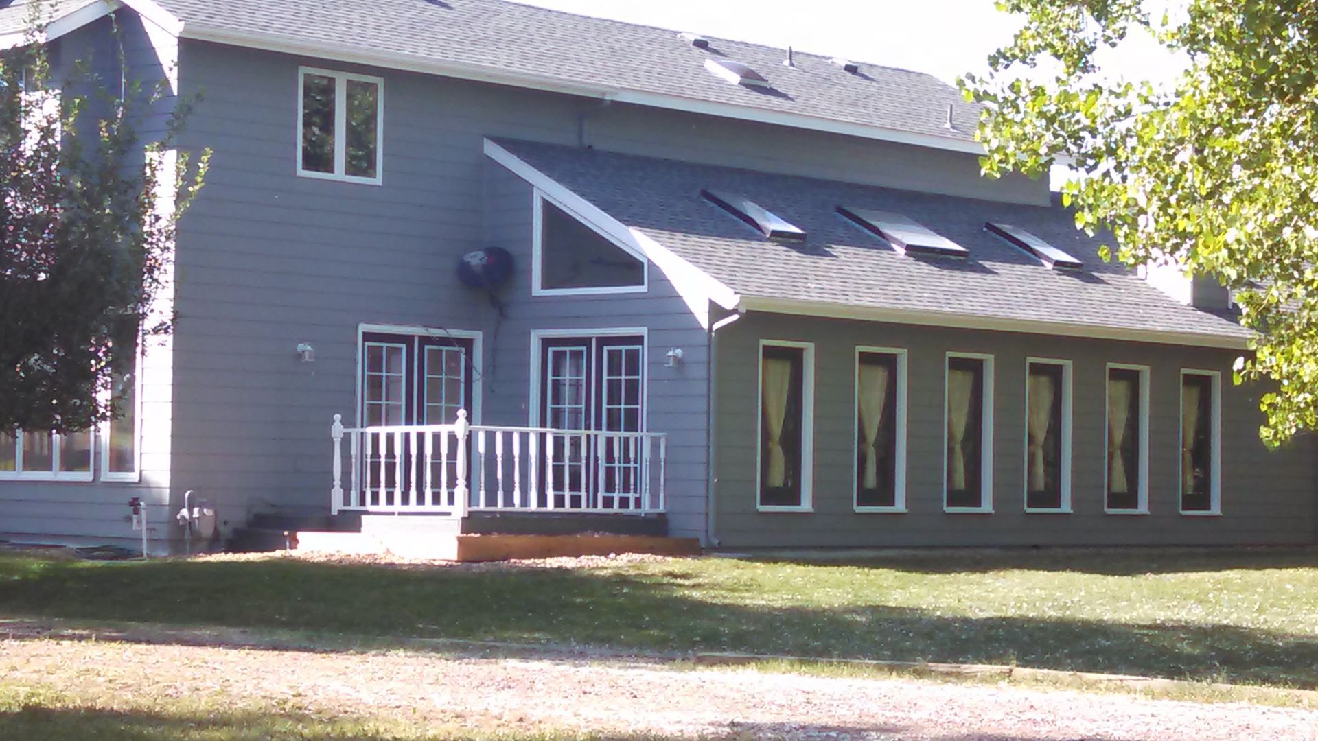 Blue-gray house with white trim, porch, and large windows in a grassy yard.