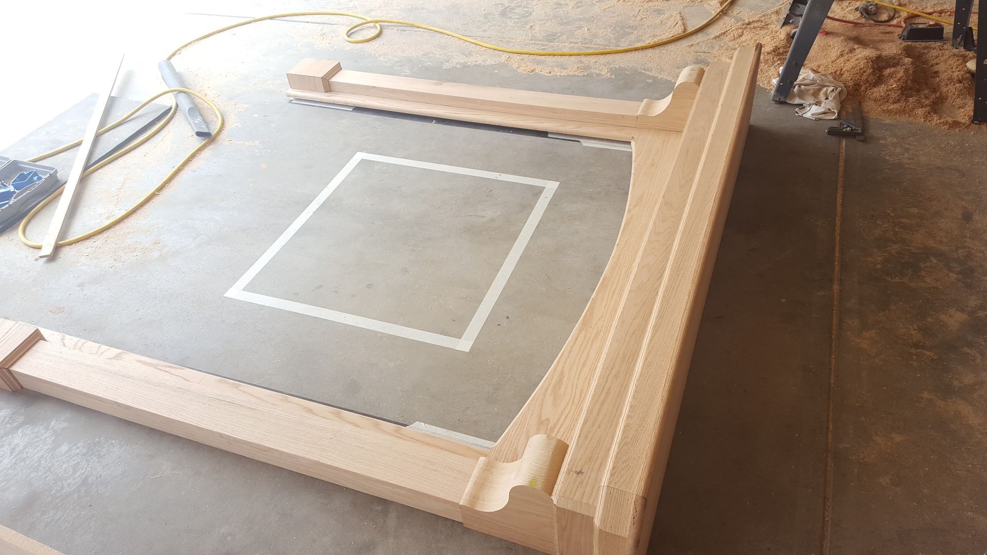 Wooden frame around a gray work surface with a white square marking, in a workshop.