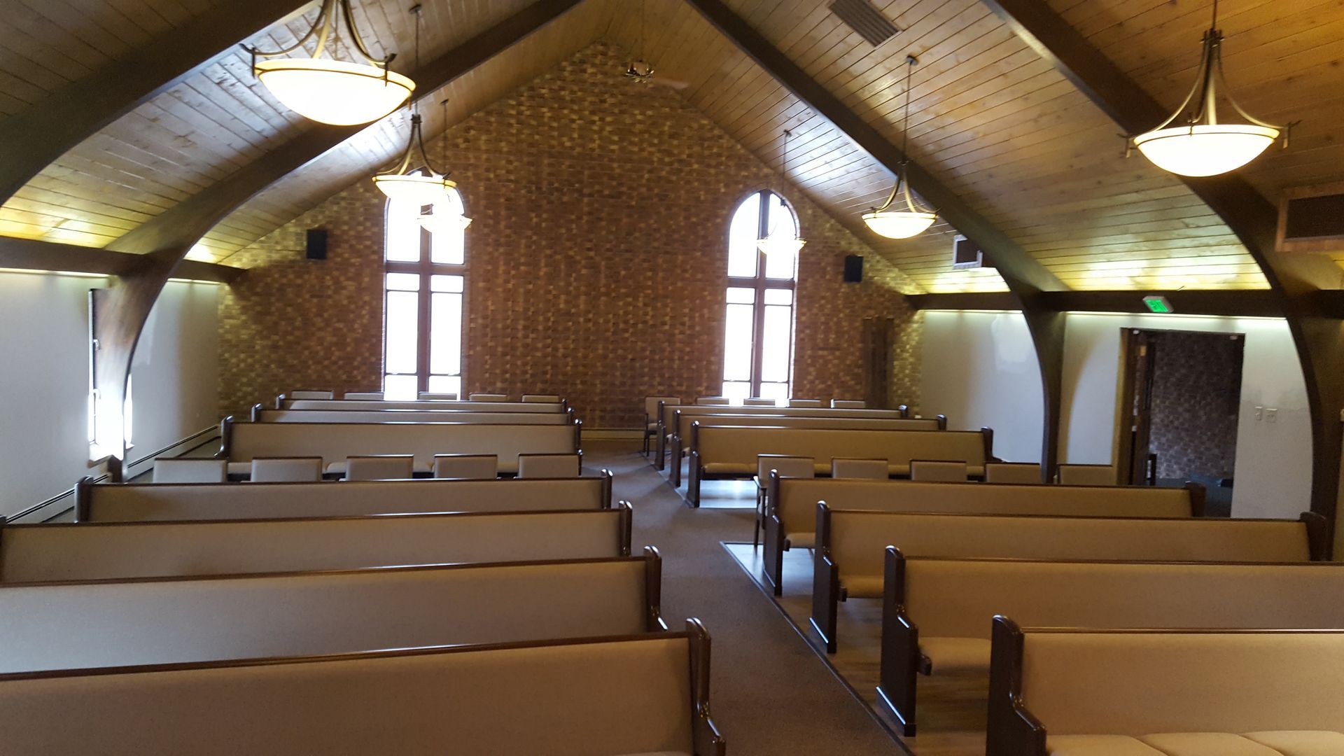 Empty church interior with wooden pews, arched windows, and hanging lights.