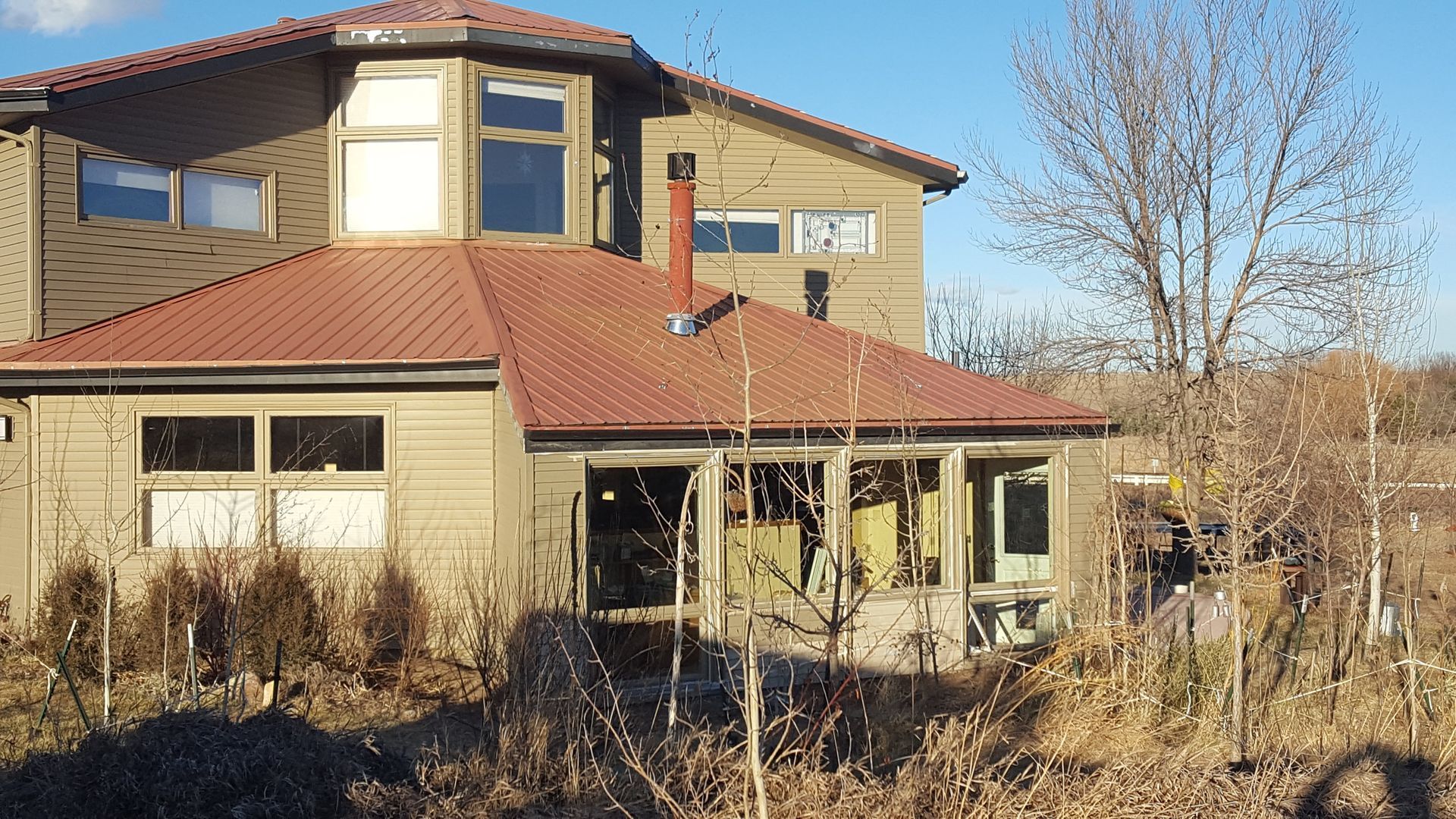 Two-story tan house with red roof, front porch, and leafless trees in a winter yard.