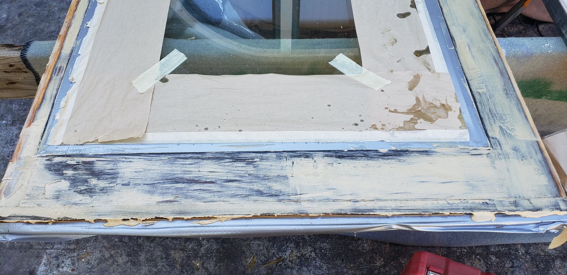 Close-up of a weathered white window frame with peeling paint and taped glass panels.