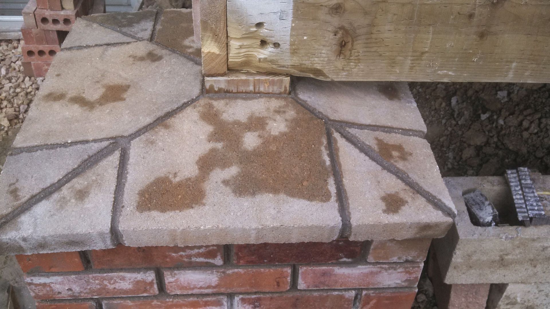 Stone paving slabs on a brick base under a wooden beam, with wet stains and gravel nearby.