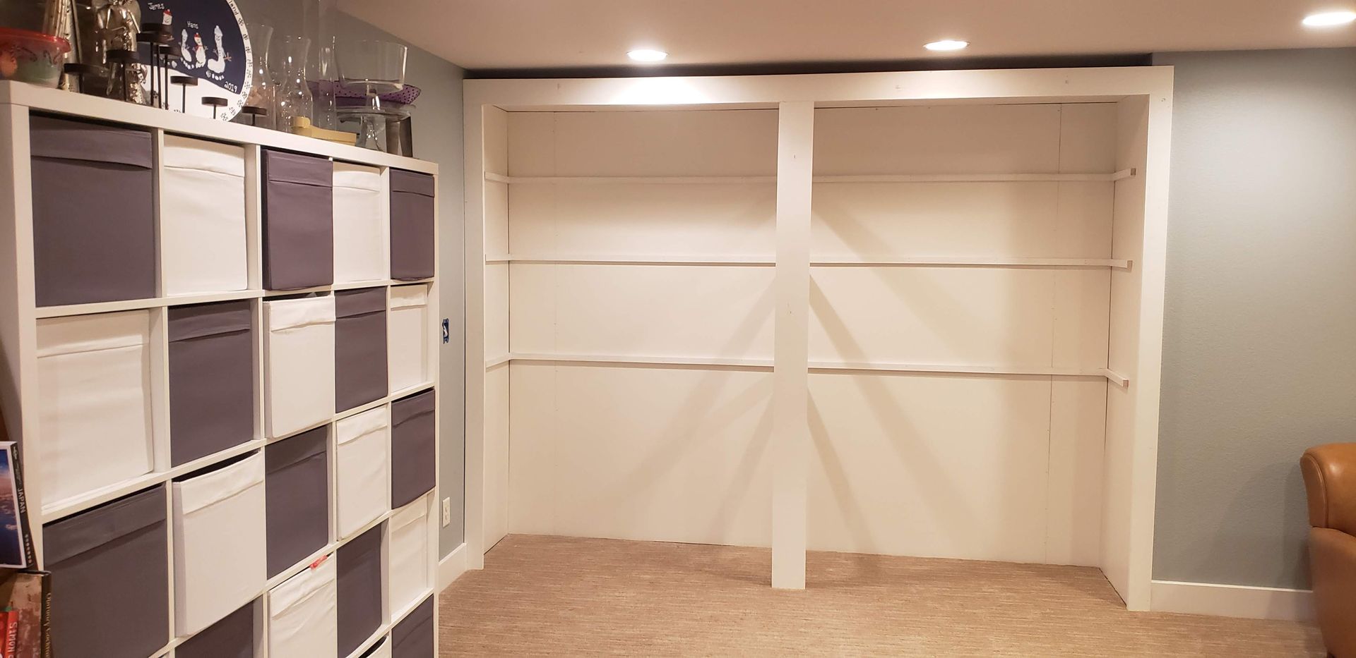 Built-in closet shelves and cubbies in a carpeted room with beige walls and folded white divider panels.
