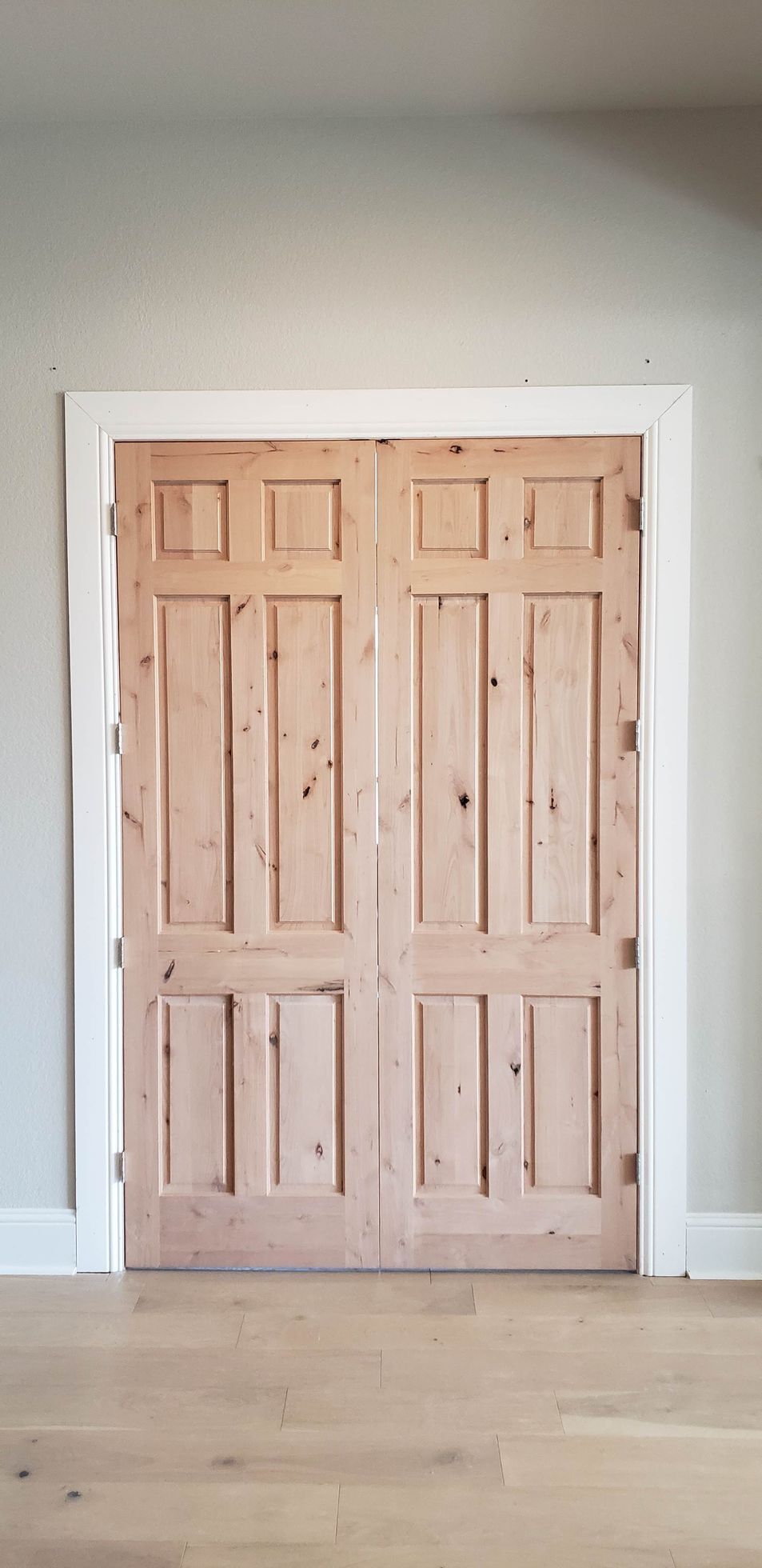 Pair of unfinished wooden closet doors in a bright, empty room with light walls and hardwood floor.