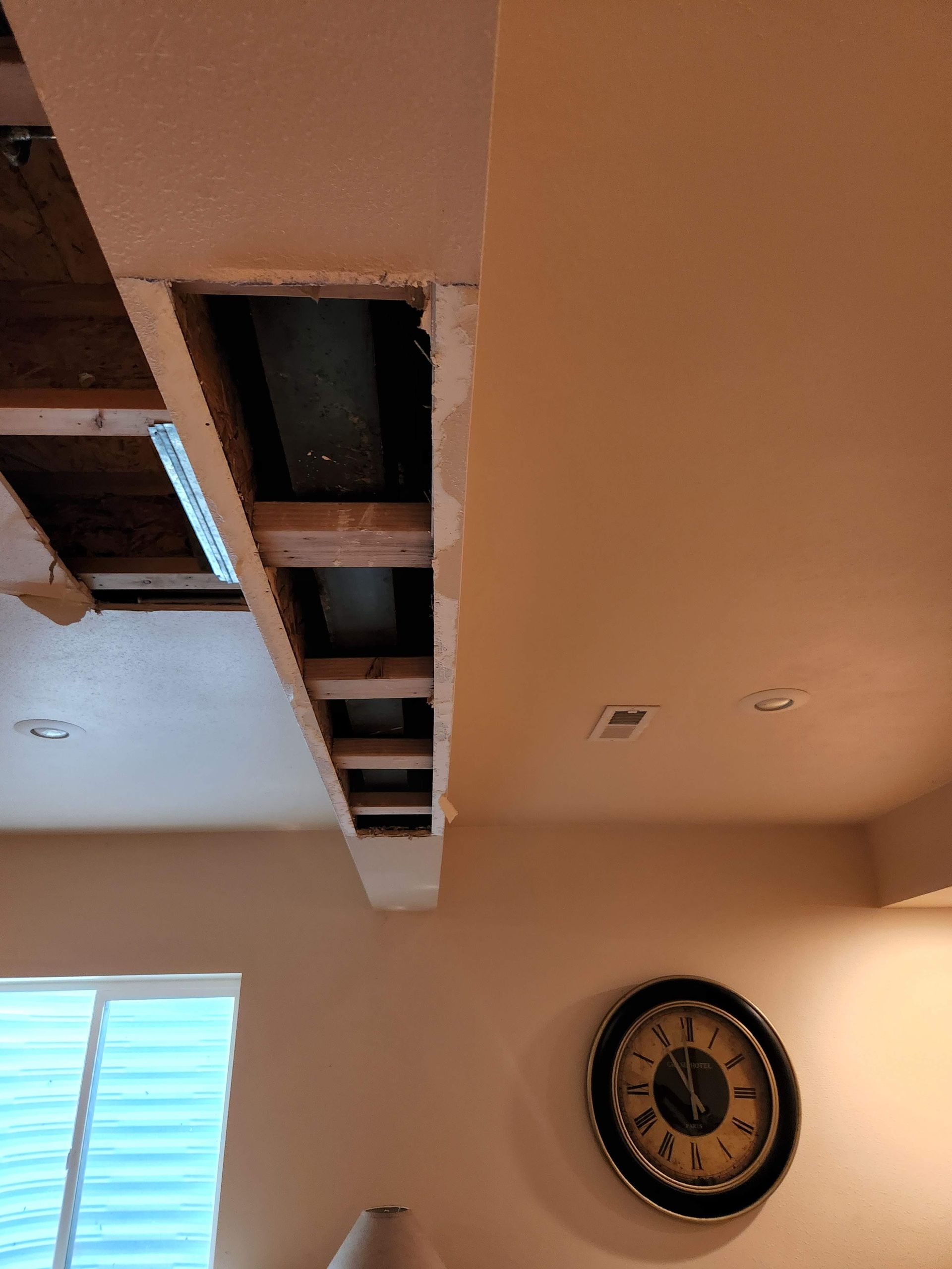 Ceiling opening with exposed wooden beams and a clock on a beige wall.
