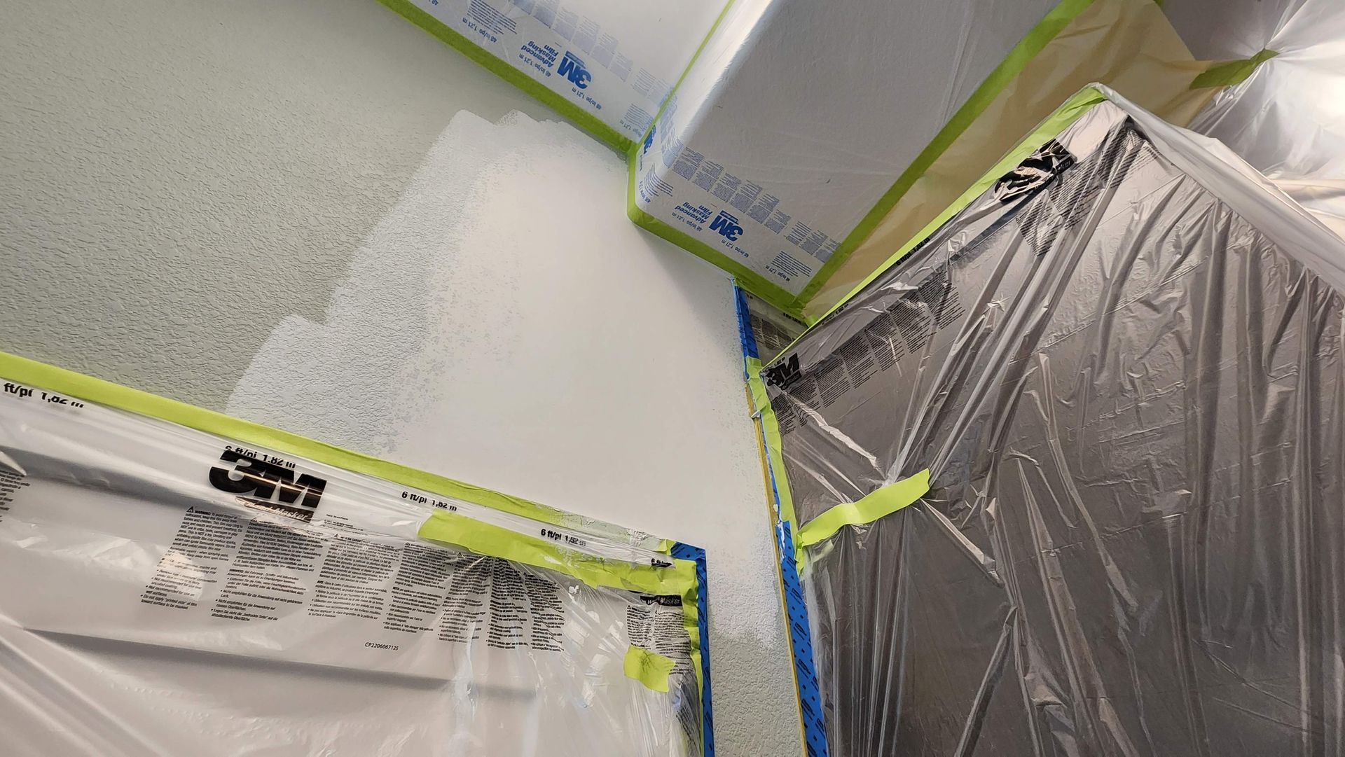 Painted room corner masked with plastic sheeting and blue painter’s tape for prep work.