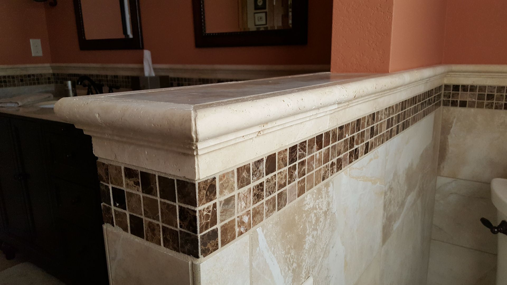 Corner tiled ledge with beige trim and brown mosaic accents in an indoor room.
