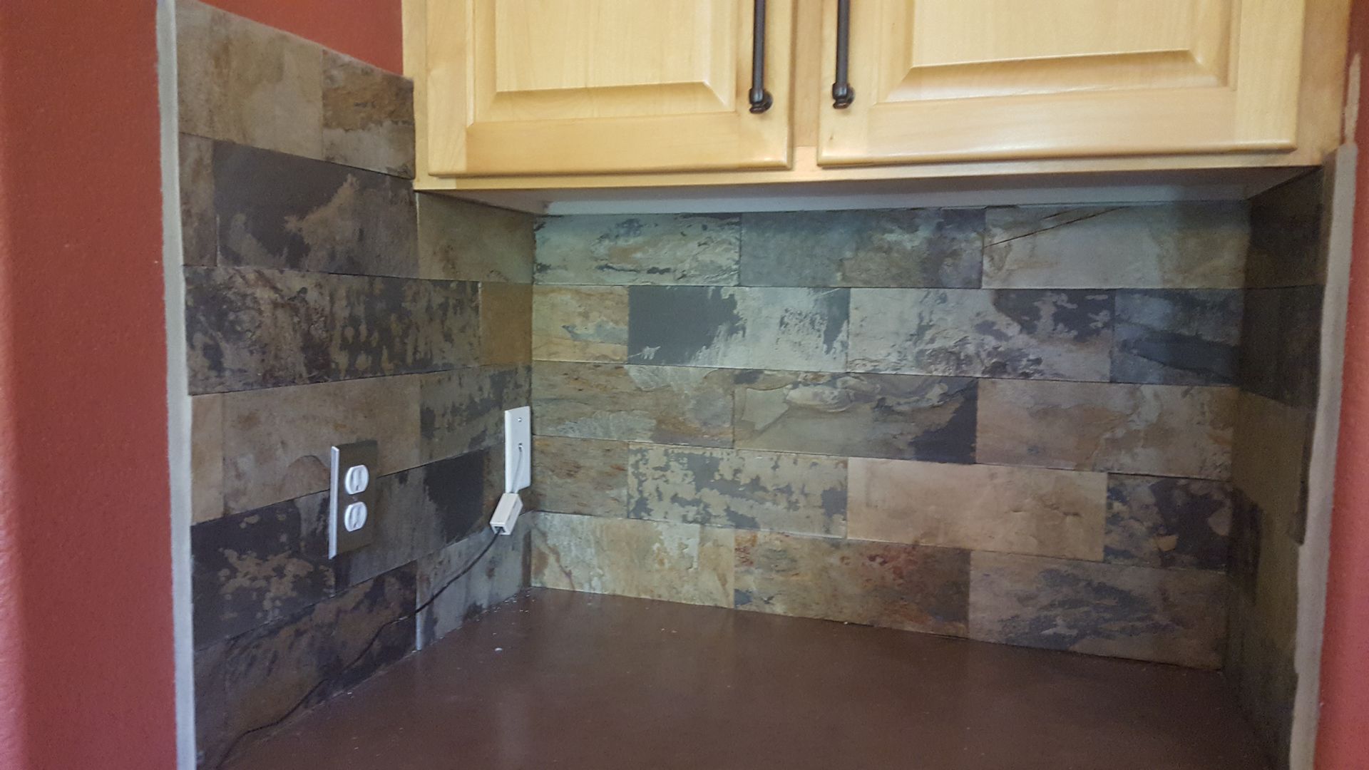Small kitchen corner with wood cabinets, stone tile backsplash, and brown countertop.