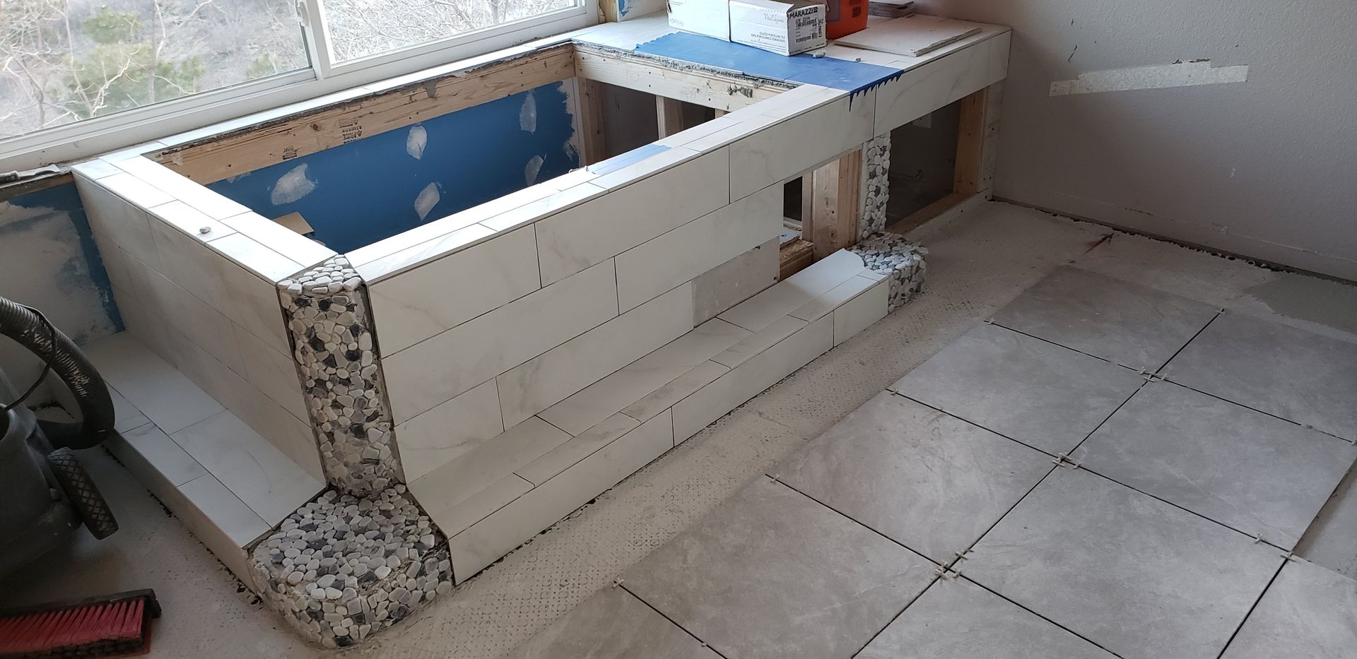 Small unfinished tiled bathroom sink with blue interior and white countertop beside a tiled floor.