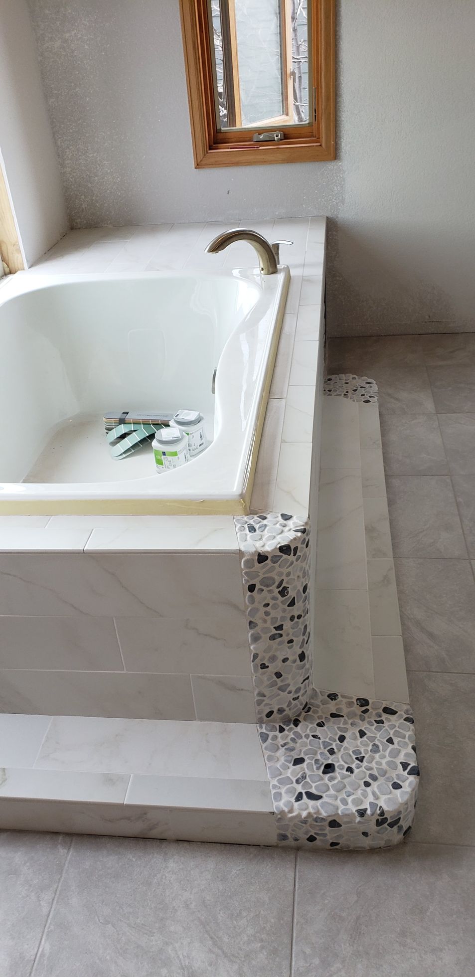 Damaged white bathtub with crumbling tile edge and loose debris in a bathroom.