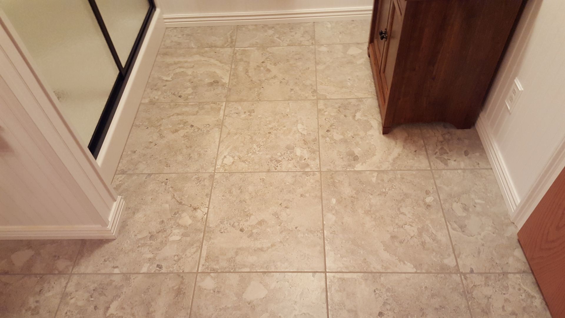 Tile floor in a hallway with white baseboards and a wooden cabinet corner on the right.