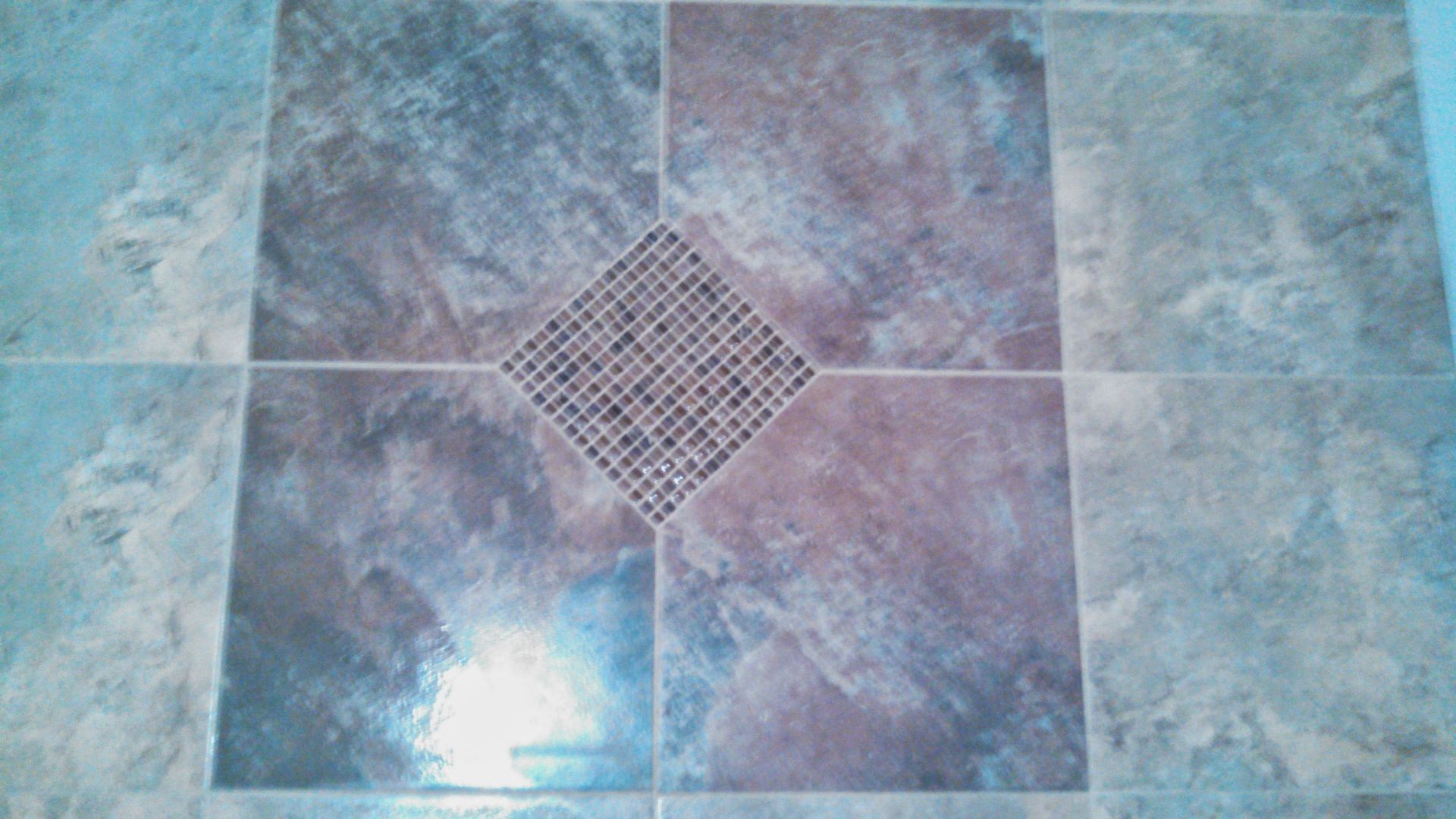Blue and gray tiled floor with a square metal drain in the center.