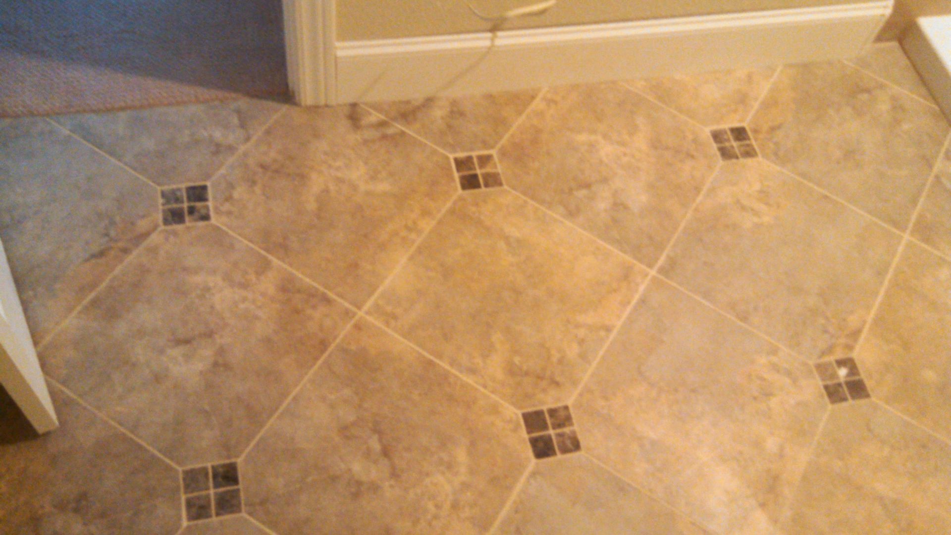 Tan tiled floor with small decorative square accents near a wall and baseboard.