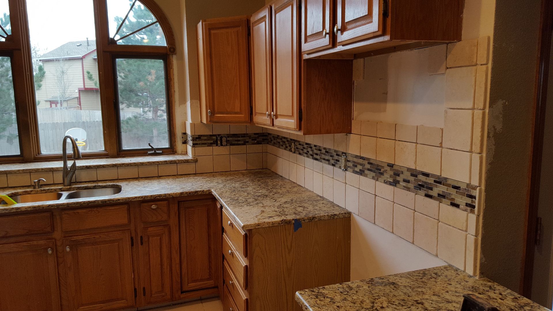 Empty kitchen with wooden cabinets, granite countertops, and a tiled backsplash by a window.