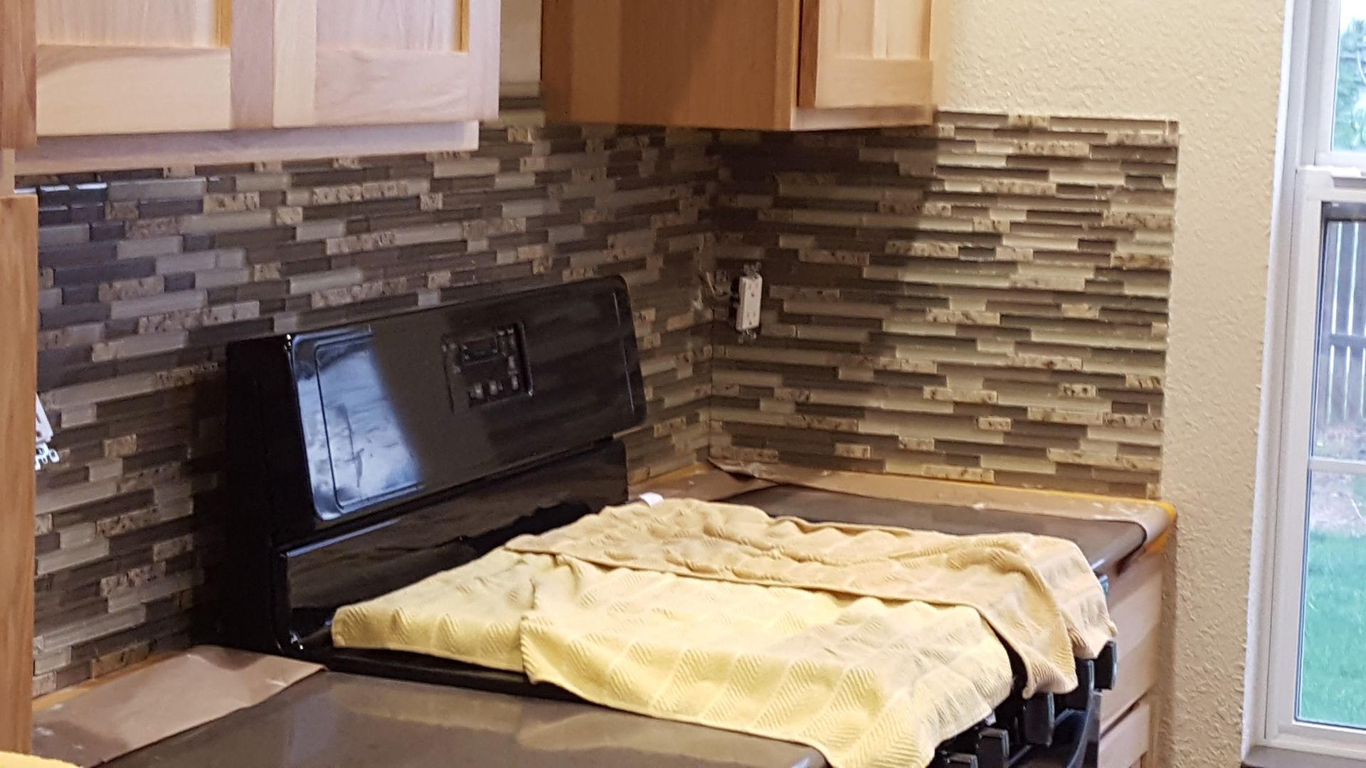 Kitchen stove covered with a cloth, under wood cabinets and a tiled backsplash.