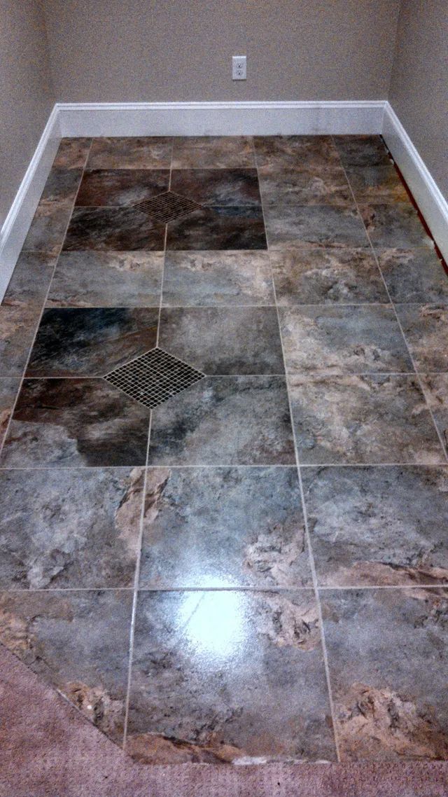Empty room with glossy multi-color tile floor and a small square drain in the center.