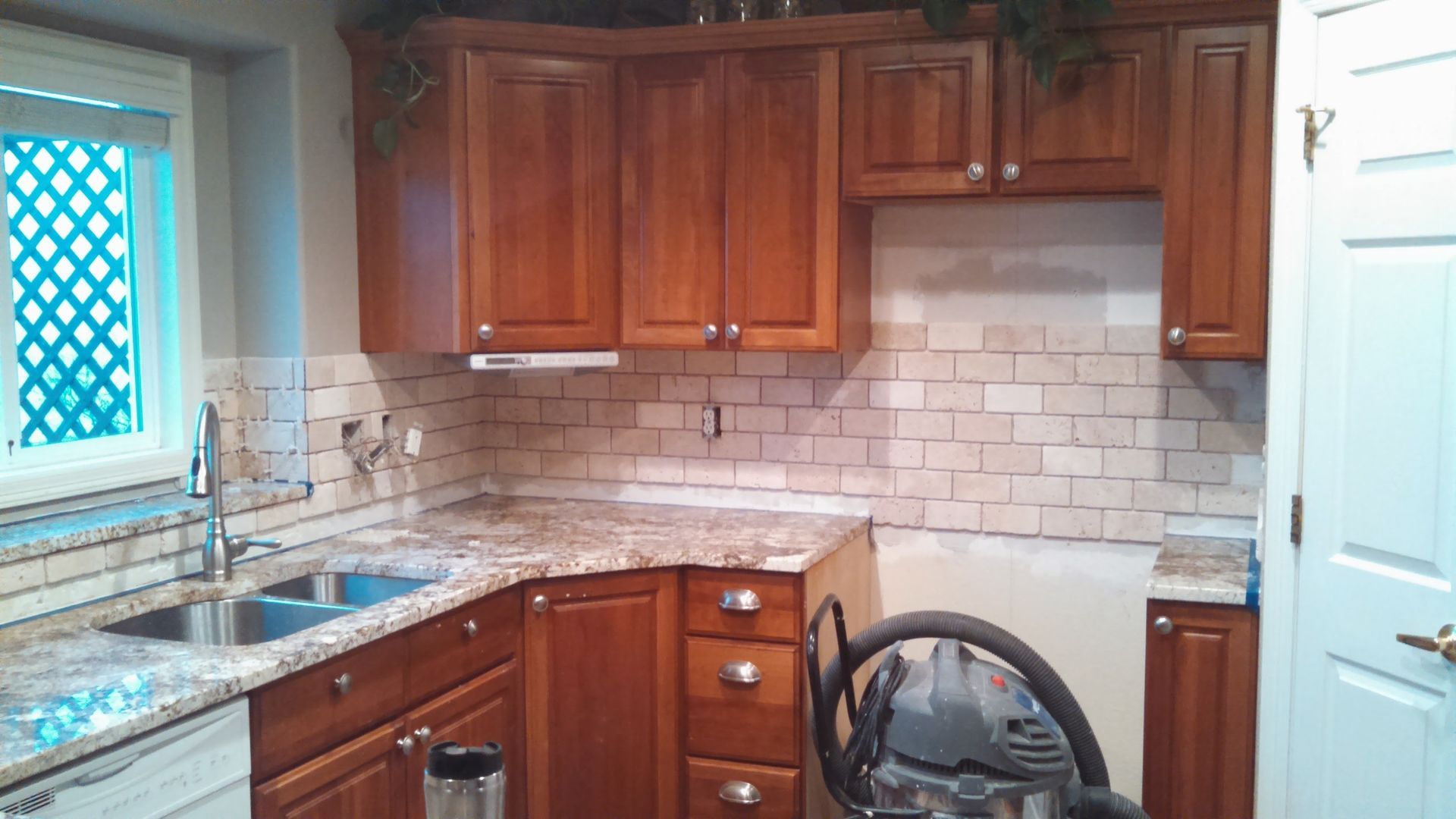Kitchen with wood cabinets, white subway tile backsplash, sink by window, and a stroller near the counter.