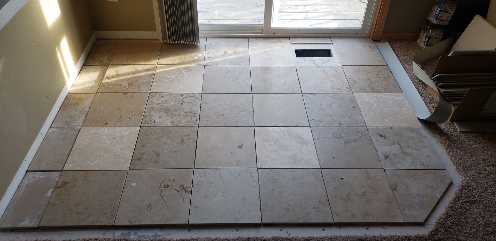 Raised tile floor under construction near a bright doorway, with loose tiles and a vent opening in the center.