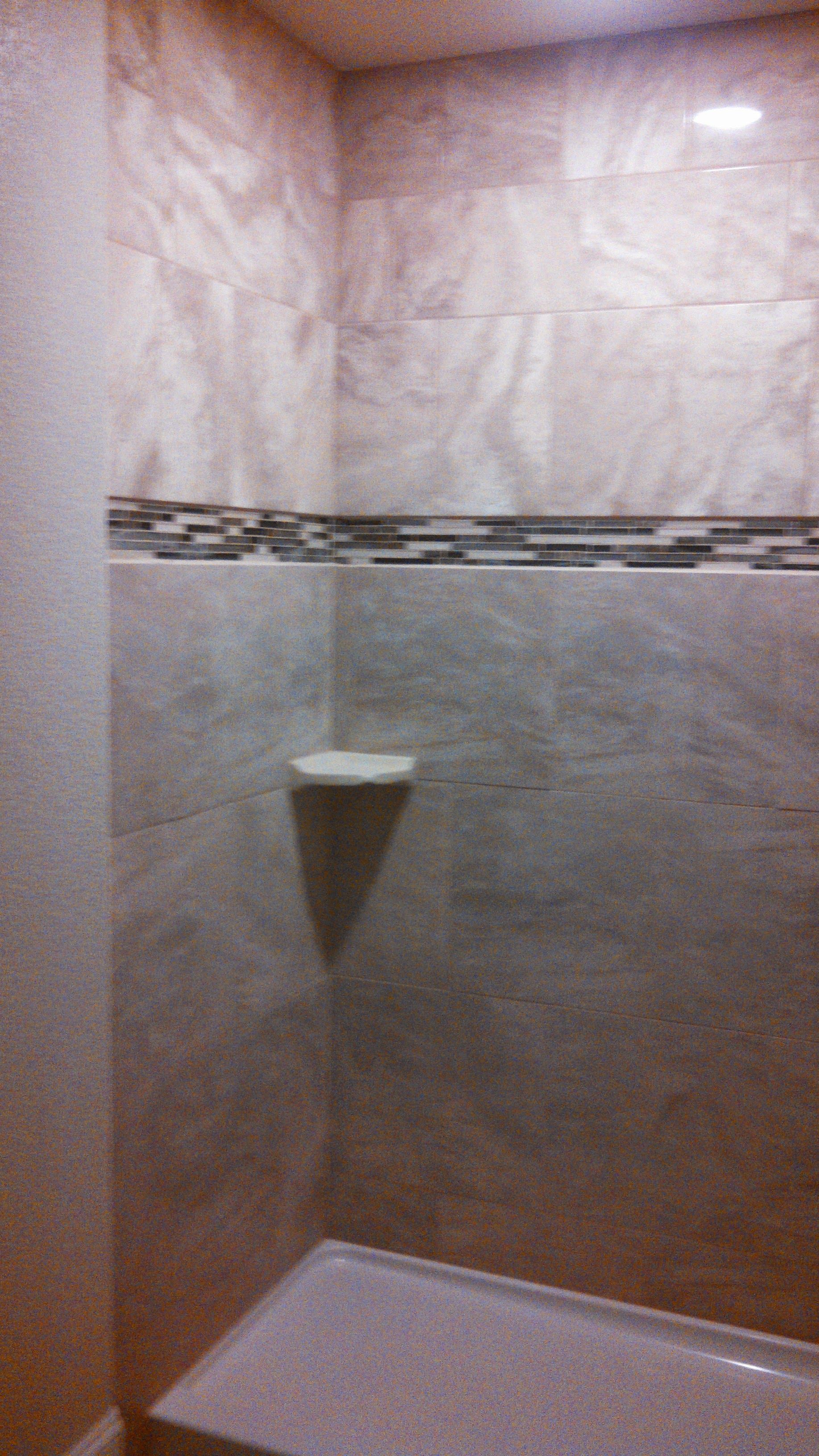 Empty tiled shower stall with a small white shelf and a dark decorative tile band.