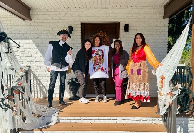 Group of five people in costumes on a porch decorated for Halloween.