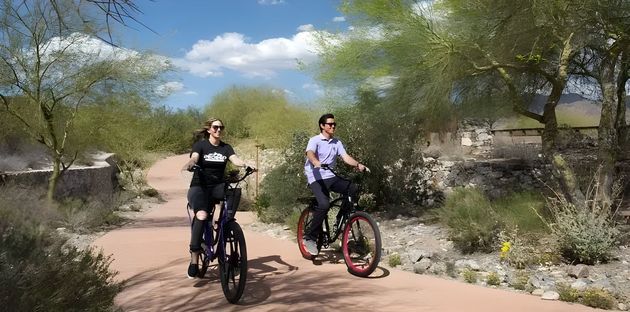 Two cyclists riding mountain bikes on a desert trail under a blue sky