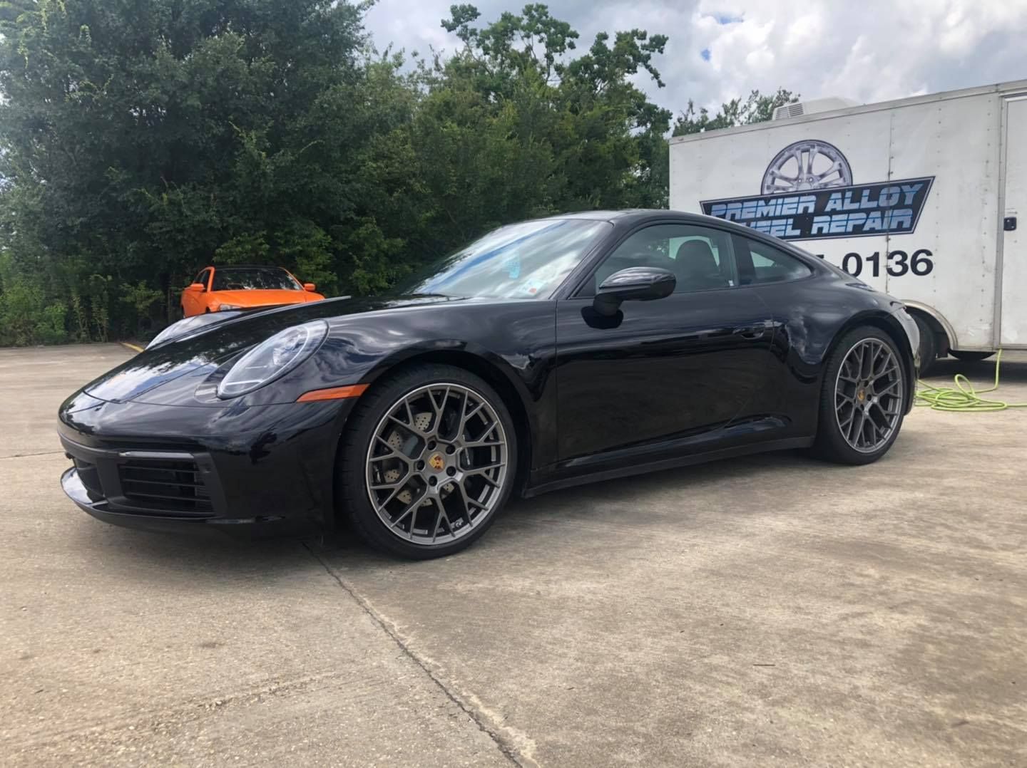 A black porsche 911 is parked in a parking lot next to a trailer.