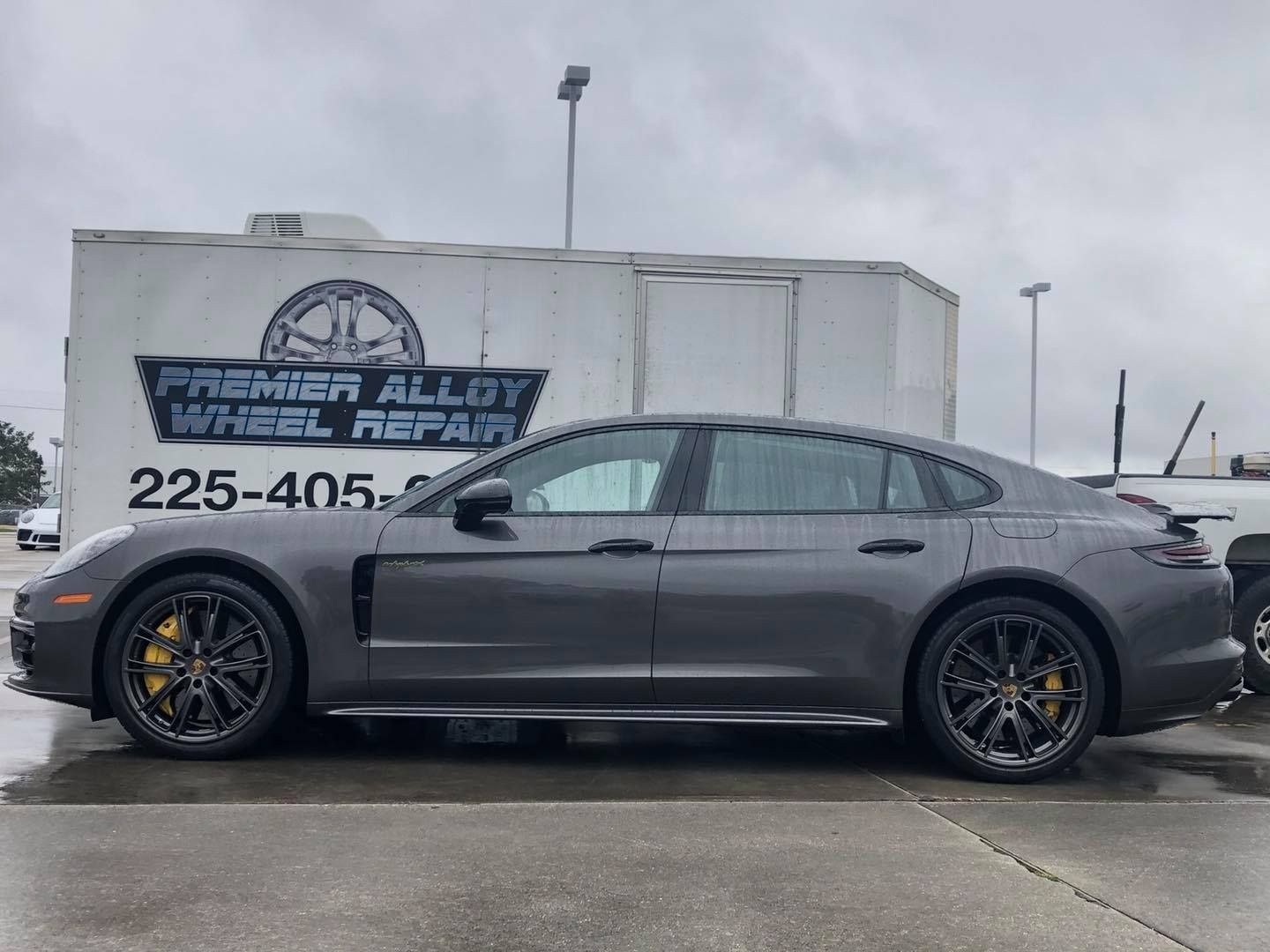 A gray car is parked in front of a white trailer.