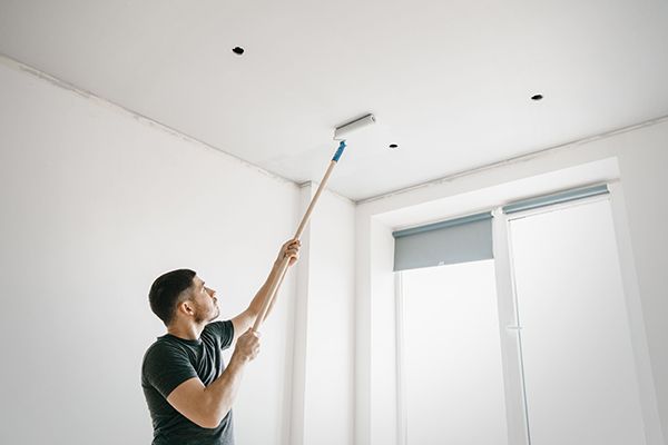 A man is painting the ceiling of a room with a paint roller.