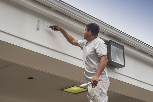 A man is painting the side of a building with a roller.