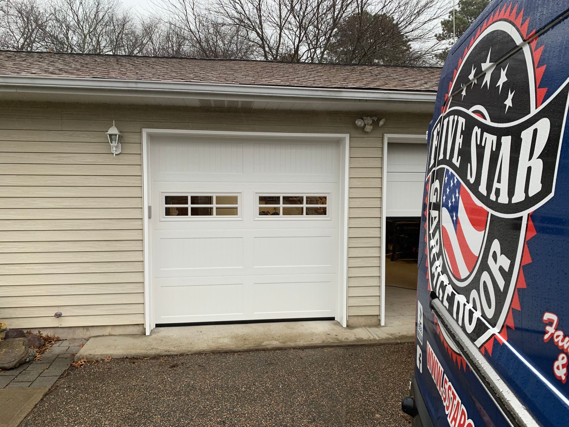 A blue van is parked in front of a white garage door.