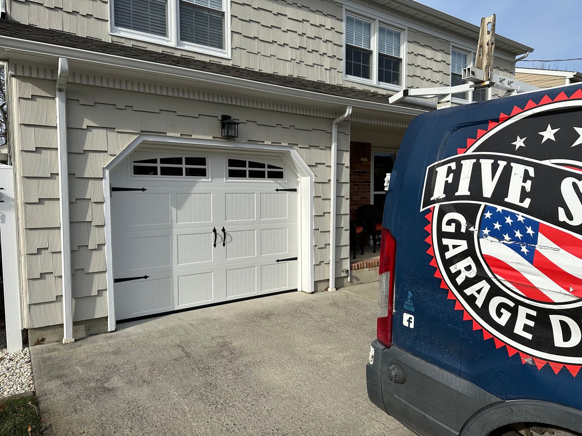 A blue van is parked in front of a white garage door.