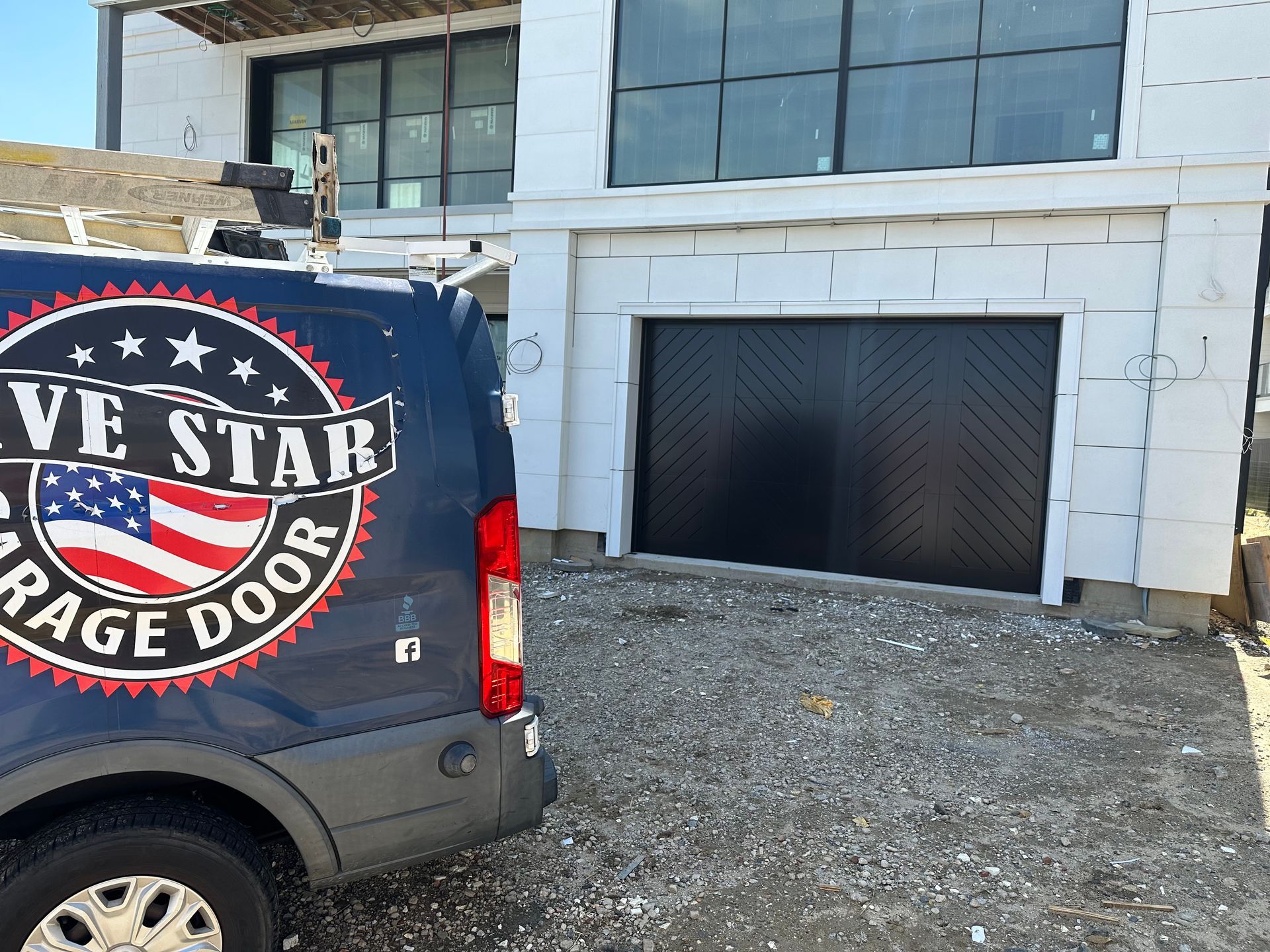 A blue van is parked in front of a garage door.