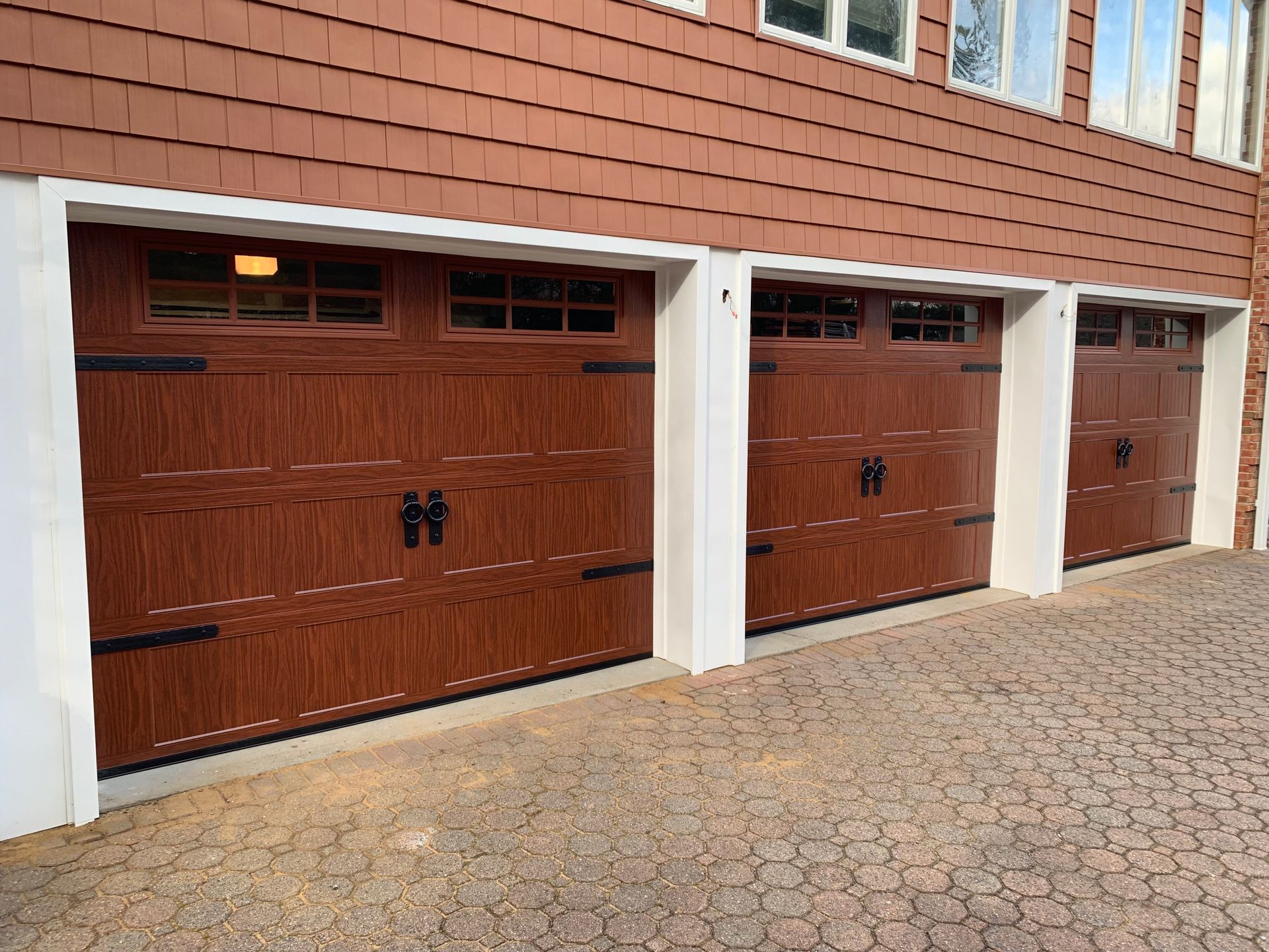 Three wooden garage doors are lined up in front of a brick building.