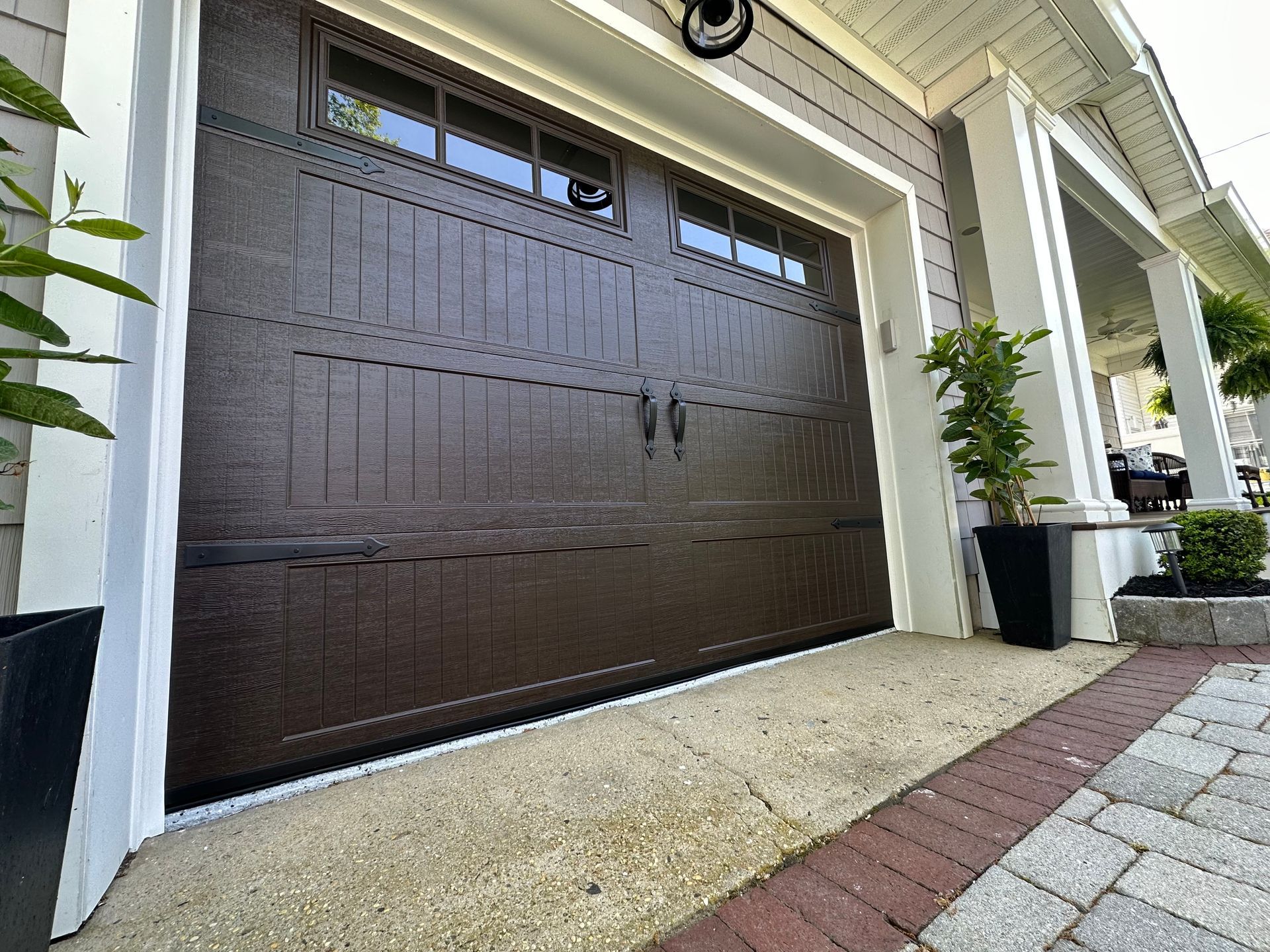 A brown garage door is sitting in front of a white house.