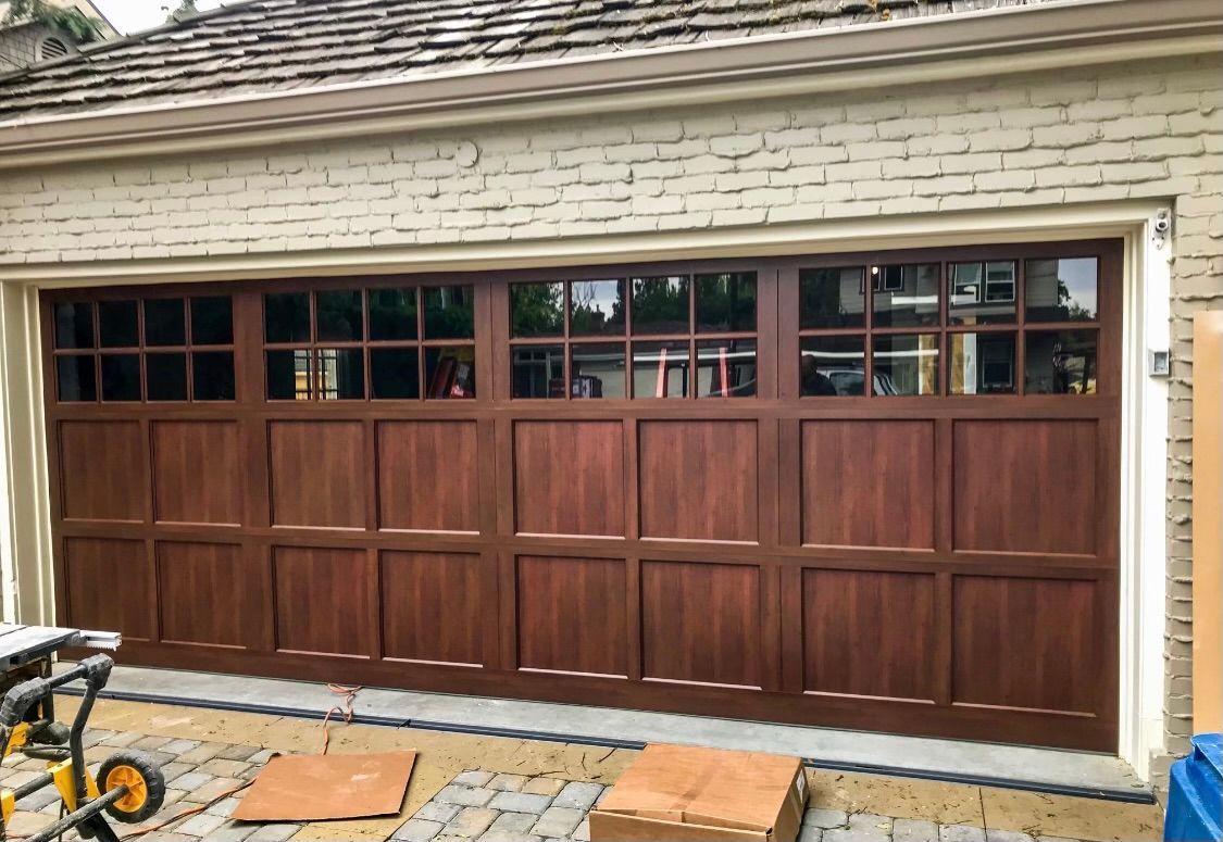 A wooden garage door is being installed on a white brick house.