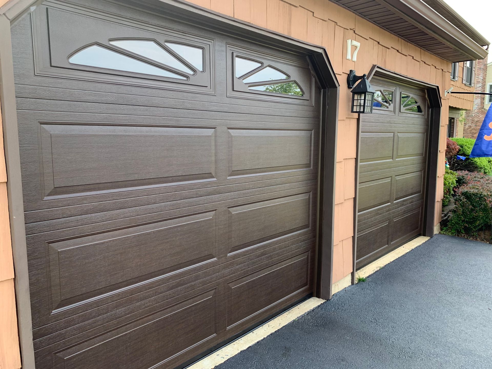 Two brown garage doors are sitting next to each other on the side of a house.
