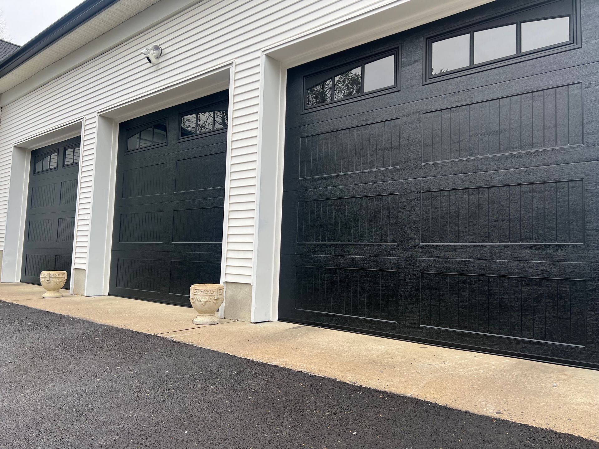 A row of black garage doors on a white house.