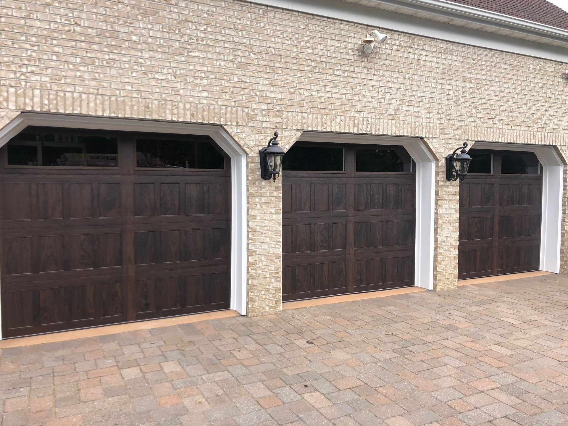 There are three garage doors on the side of a brick building.