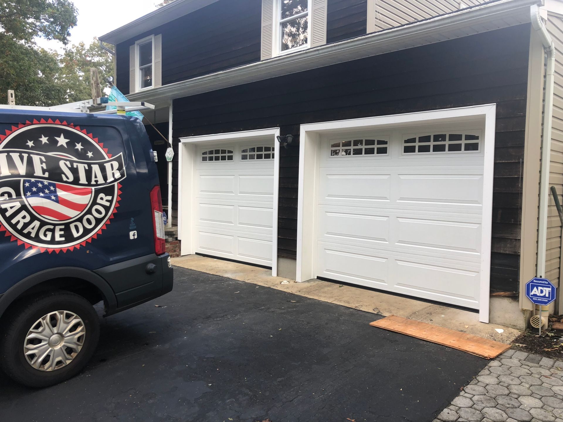 A blue van with the word garage door on it is parked in front of a house.