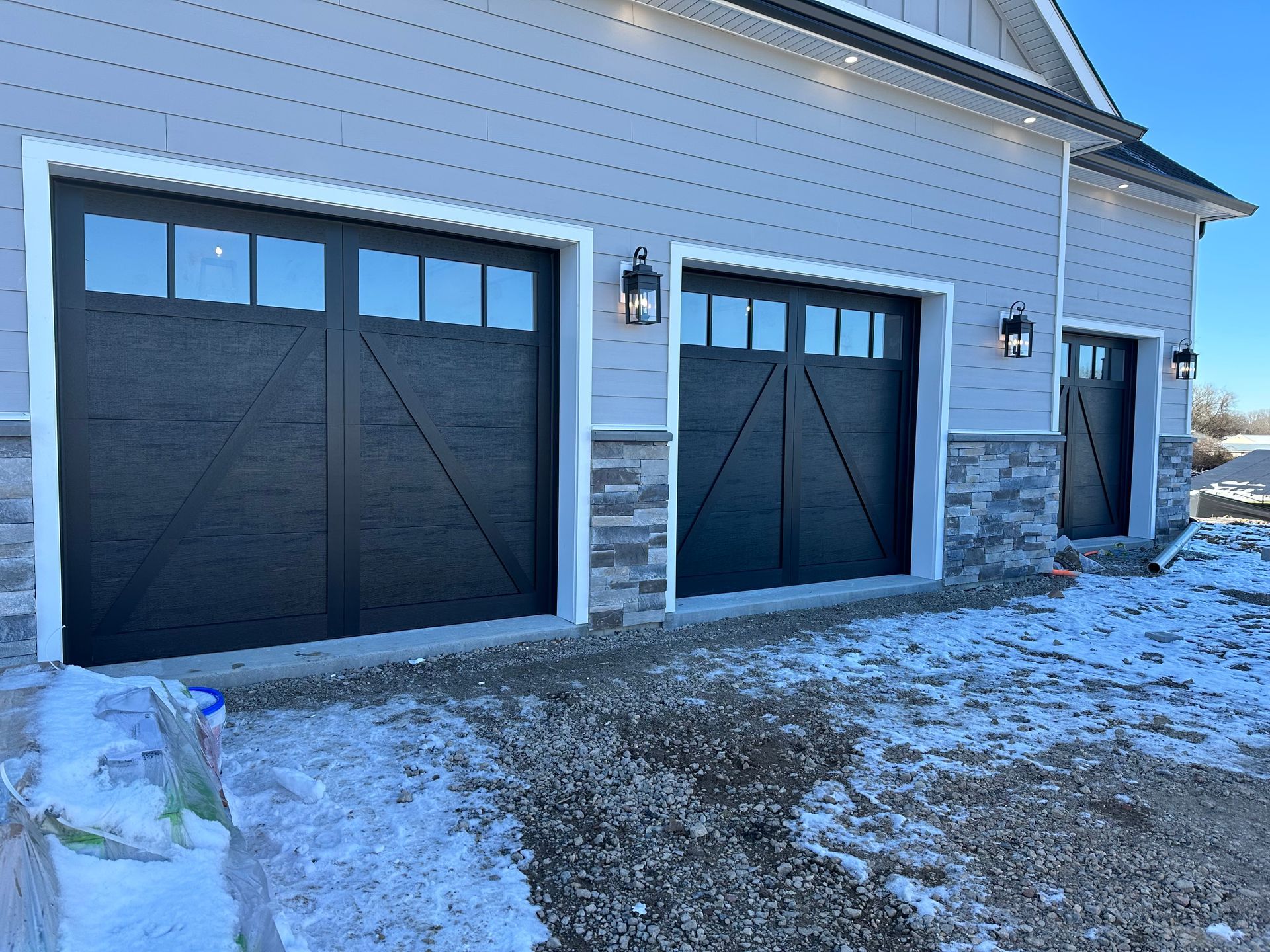 Three black garage doors are on the side of a house.