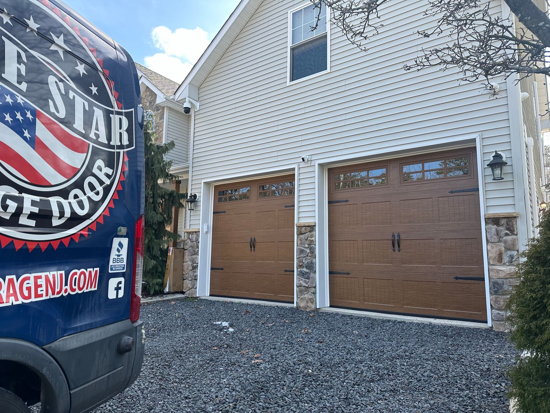 A blue van is parked in front of a house with two garage doors.
