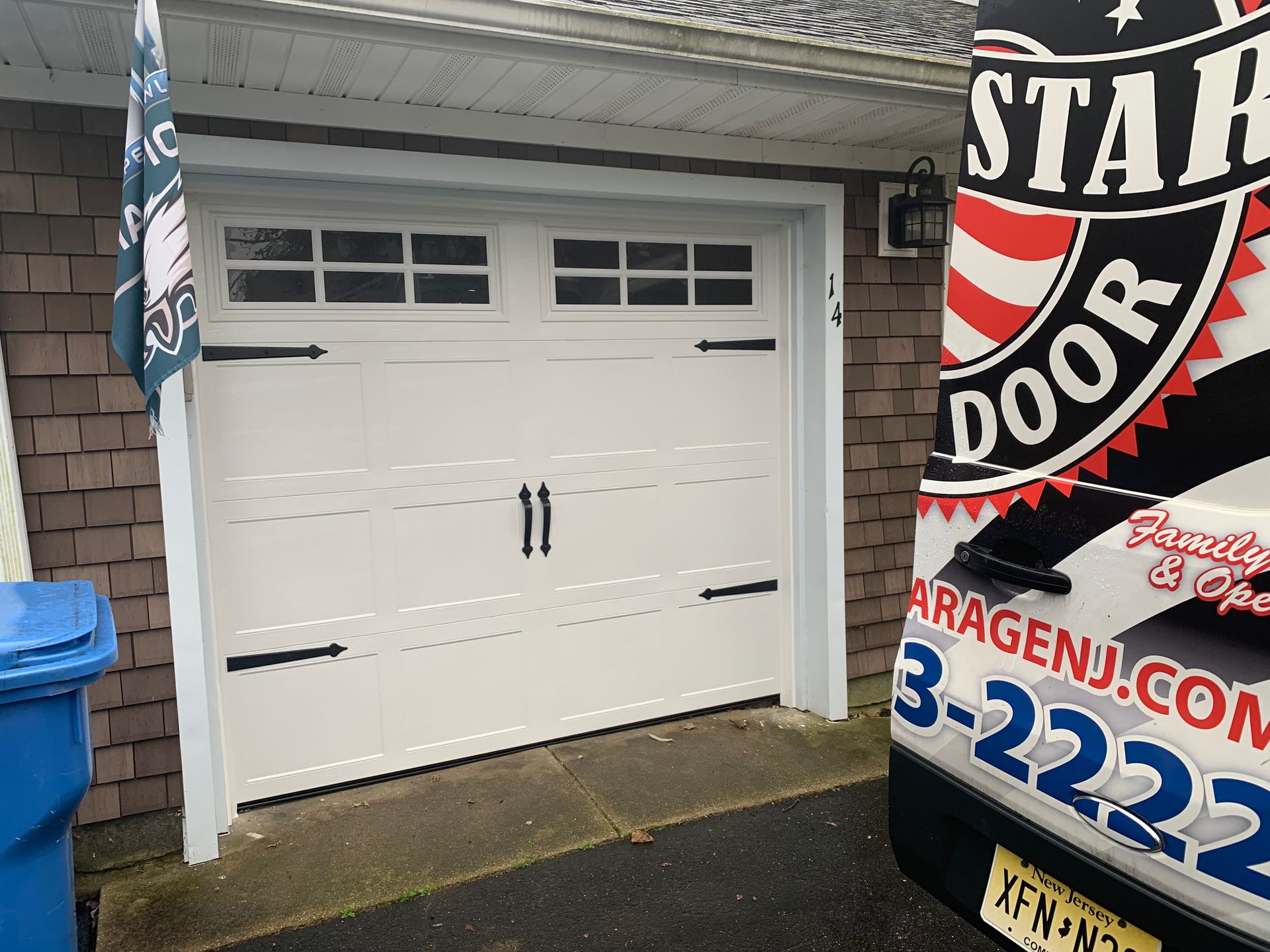 A white garage door is sitting next to a blue trash can.