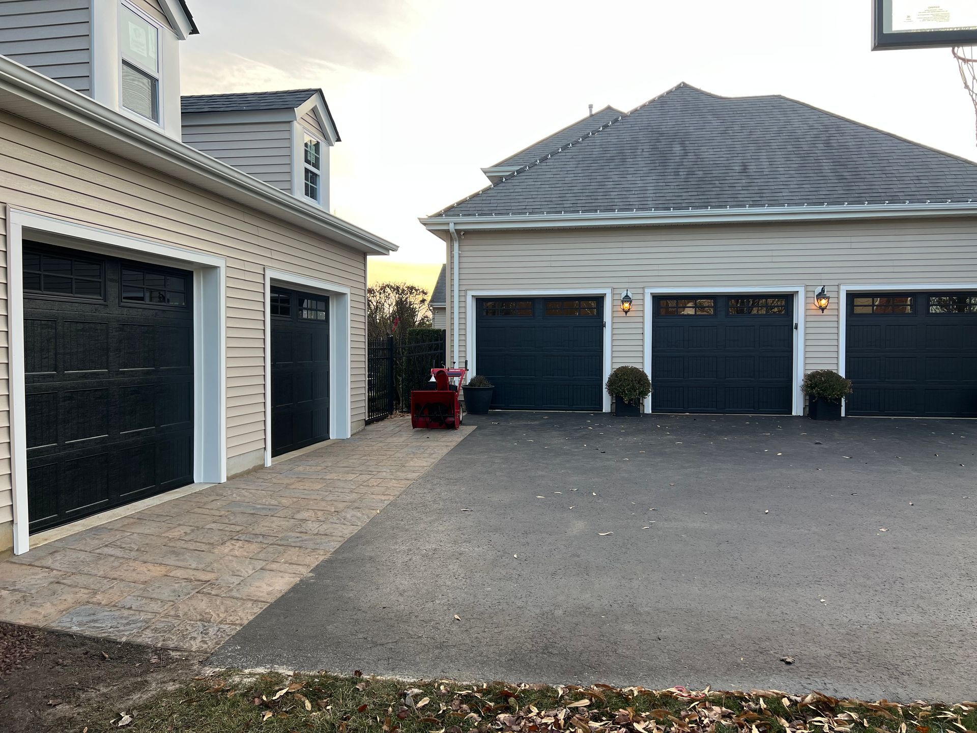 A row of garage doors next to a house with a basketball hoop in the background.