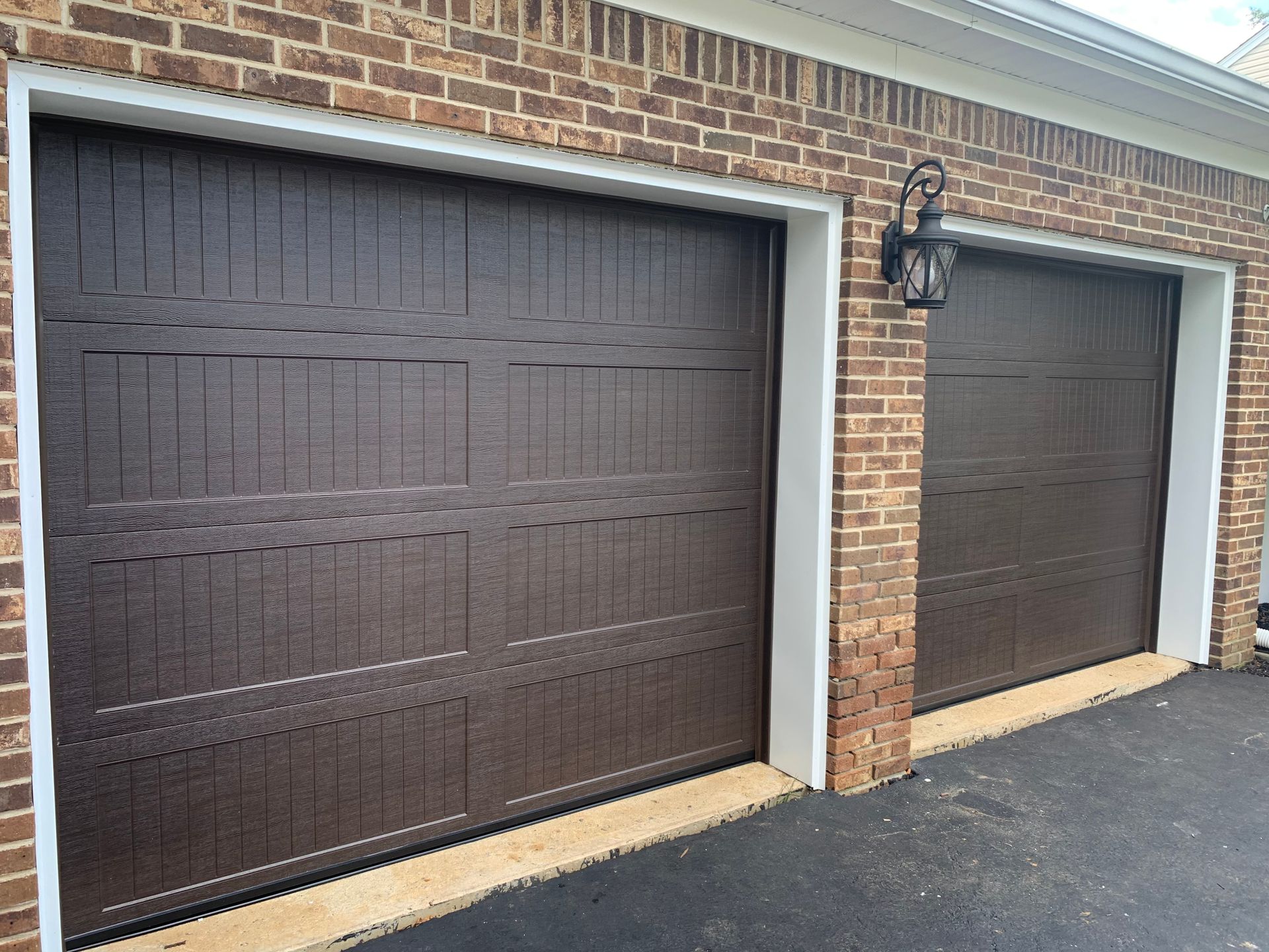 Two brown garage doors are on a brick building.