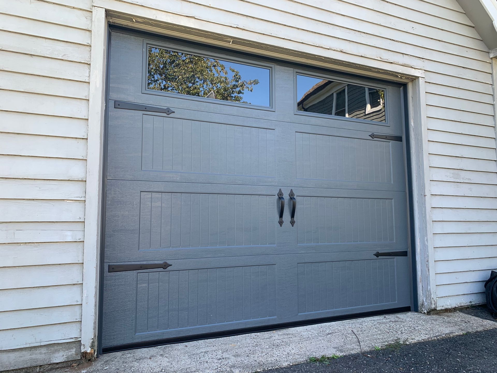 A gray garage door with a window on the side of a white house.