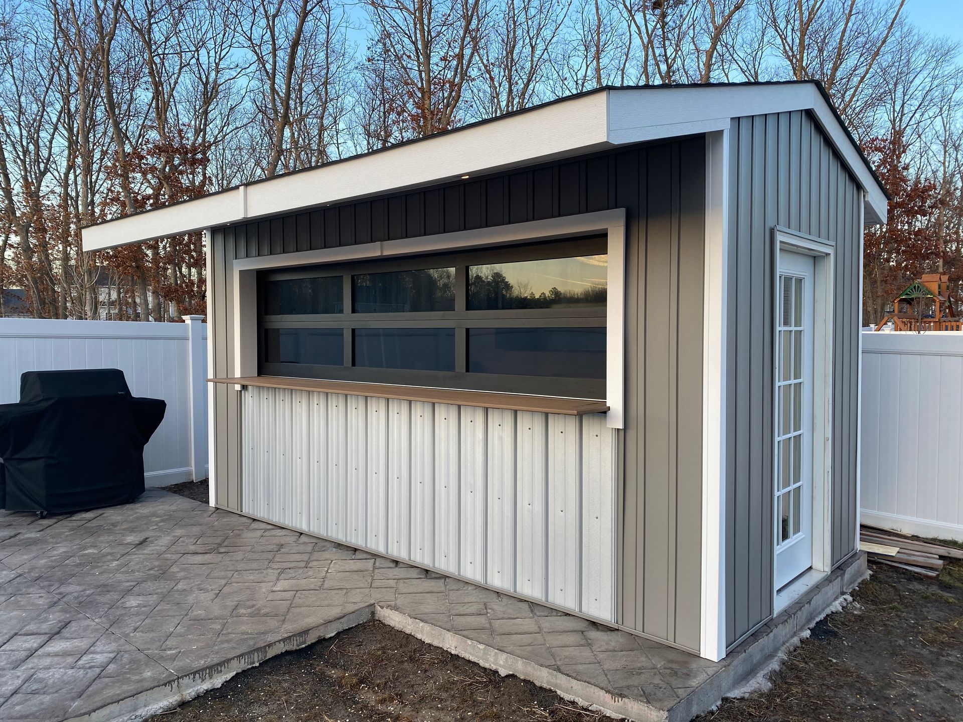 A small shed with a window and a grill in the backyard.