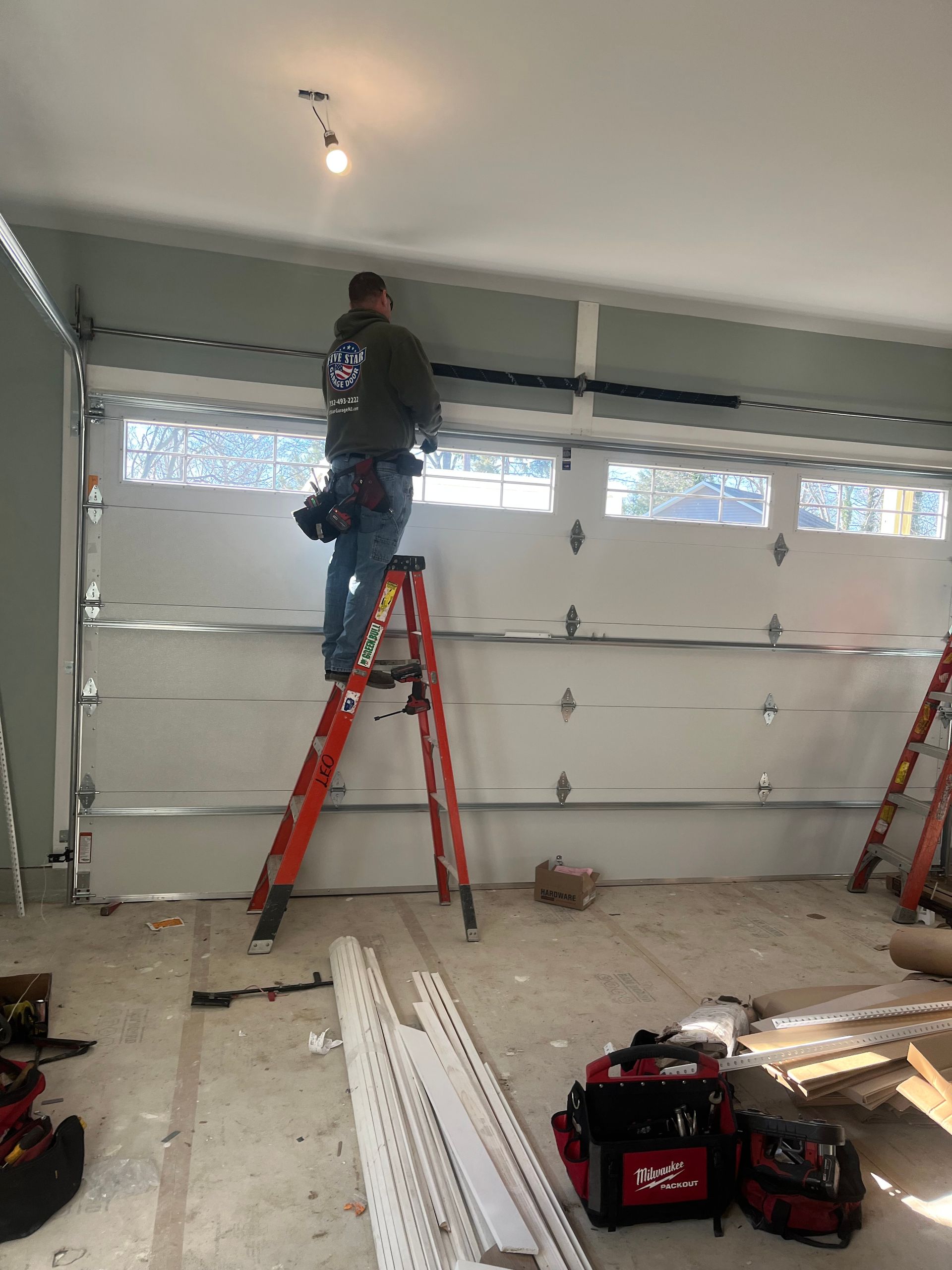 A man is standing on a ladder working on a garage door.