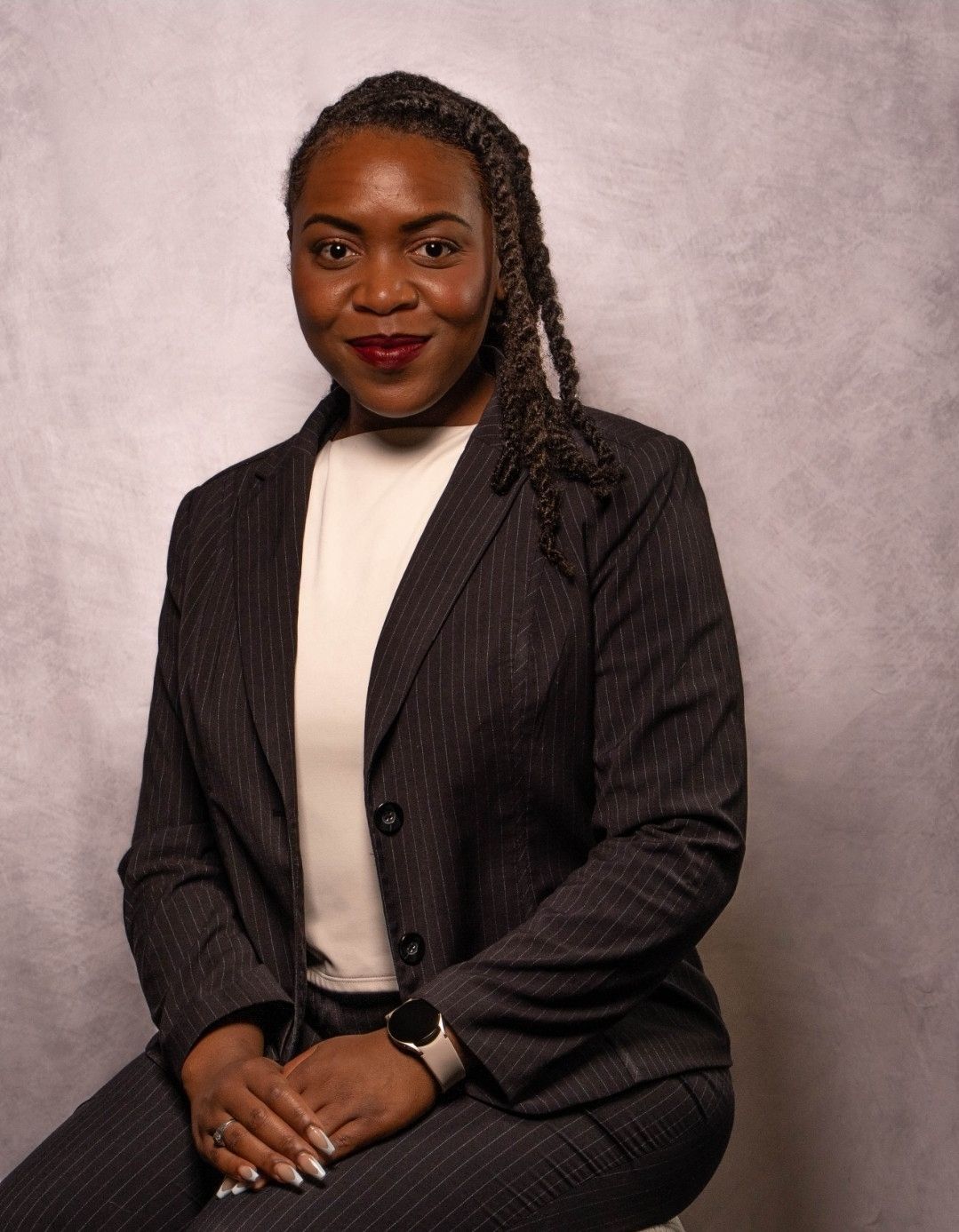 Portrait of a woman in a dark suit and white blouse, seated against a neutral backdrop, smiling gently